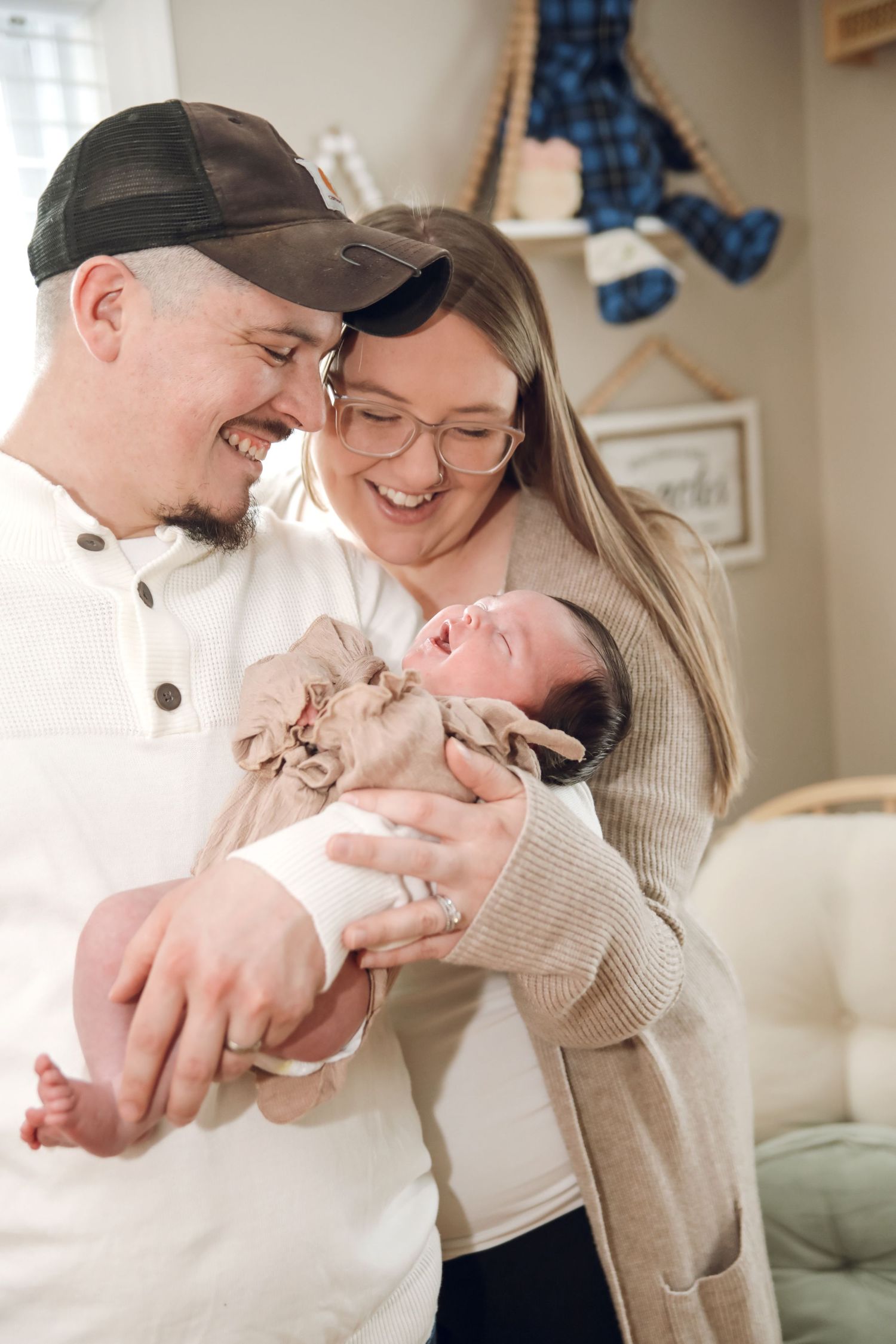 A couple in casual attire share joyful moments with their newborn baby in a cozy home setting.