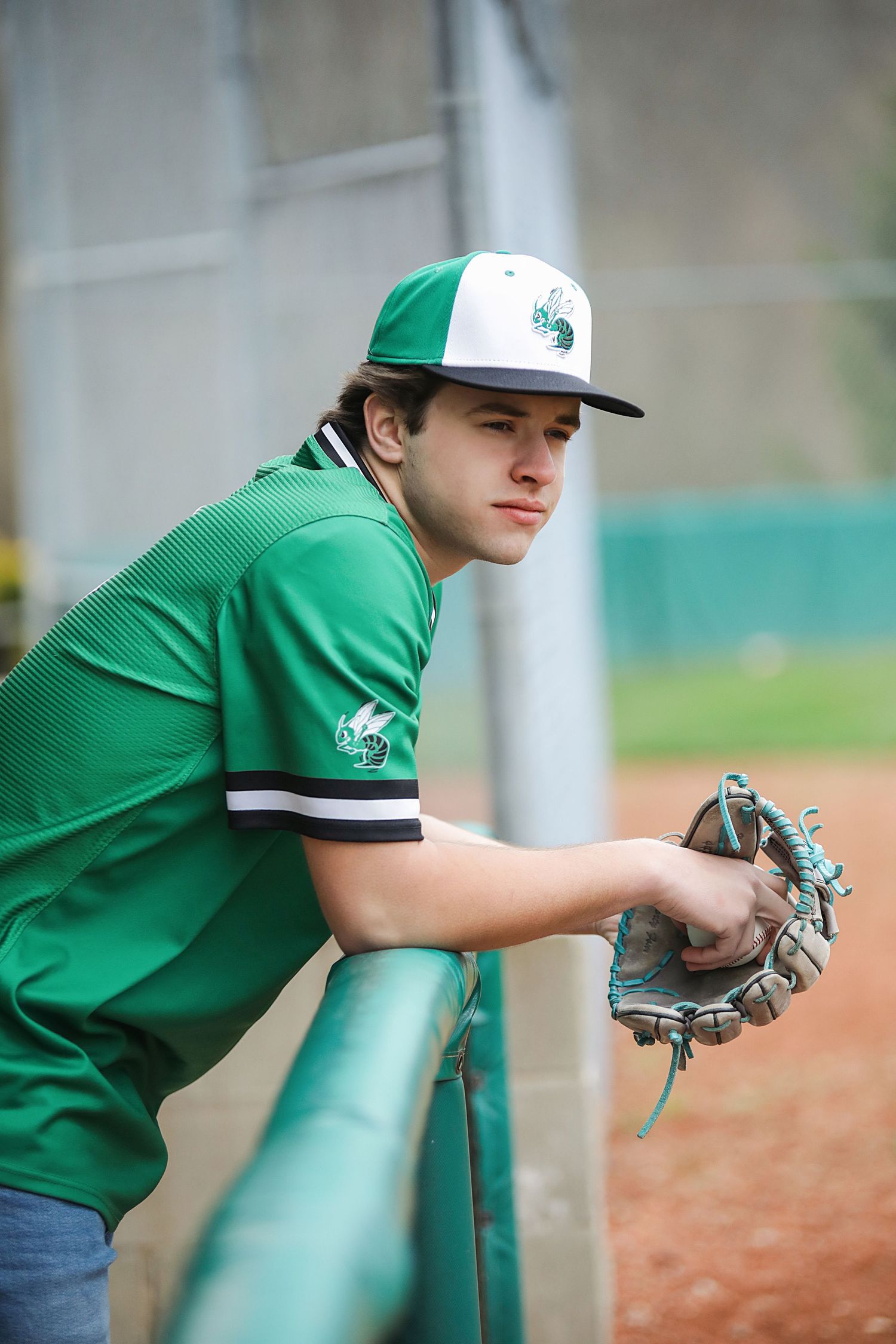 A young baseball player in green jersey practices fielding drills by crouching down with a glove at the ready.