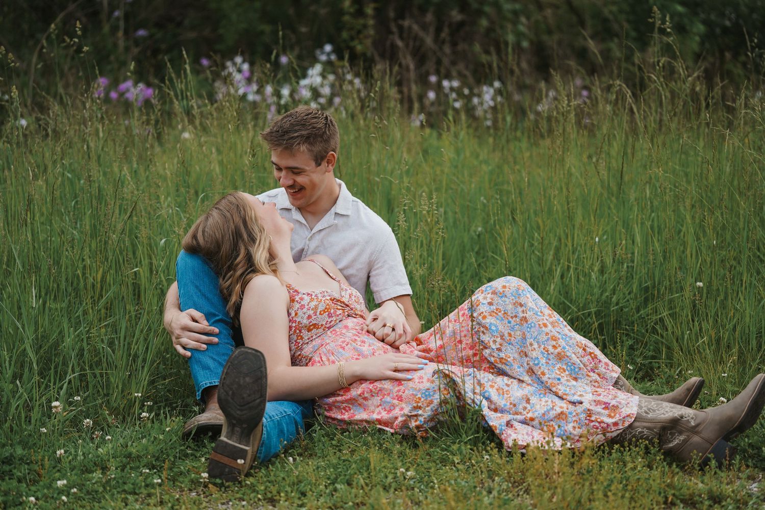 A couple shares tender moments in a green meadow at sunset wearing casual summer attire.
