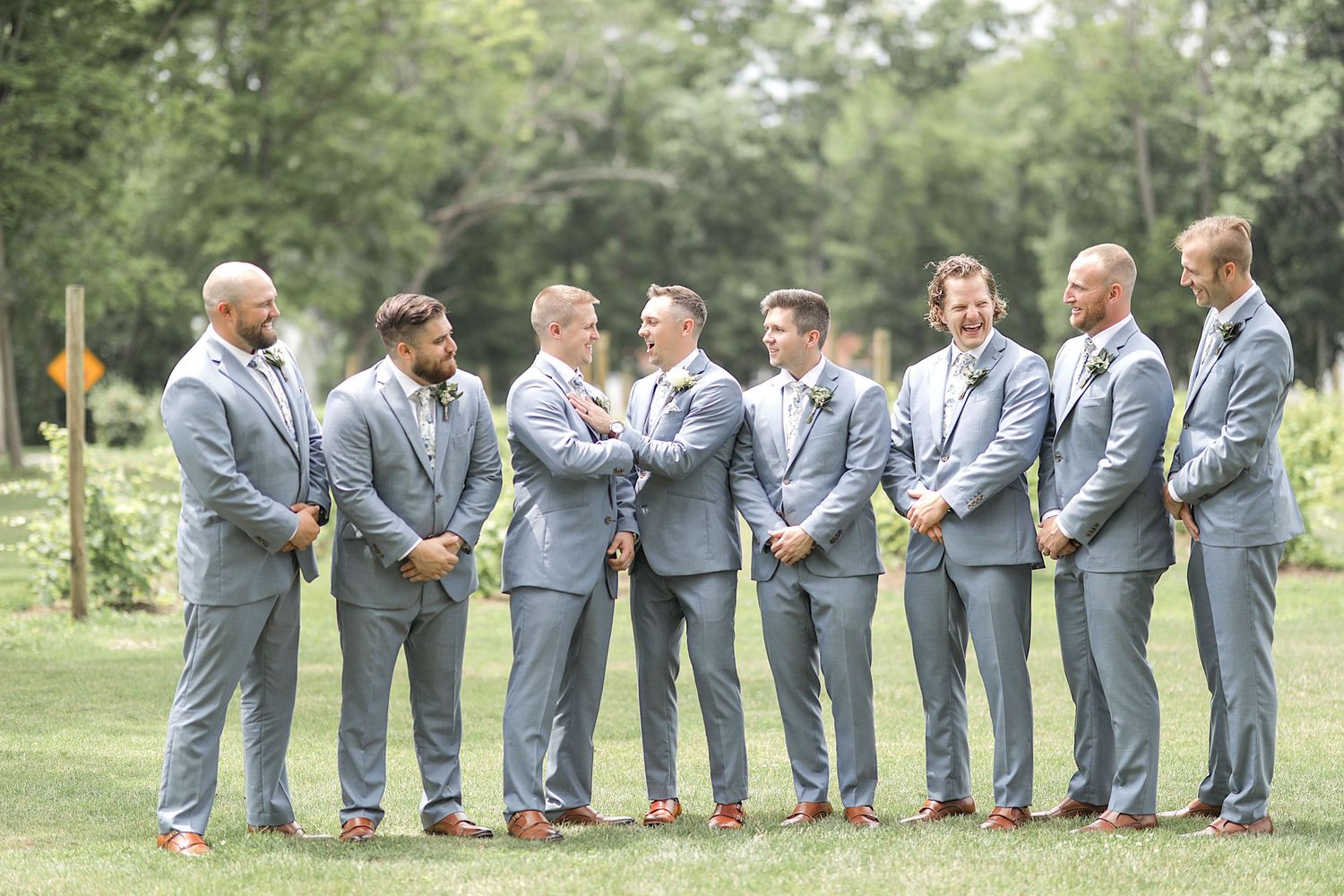 Groomsmen in matching gray suits posing together on grass at outdoor wedding venue.