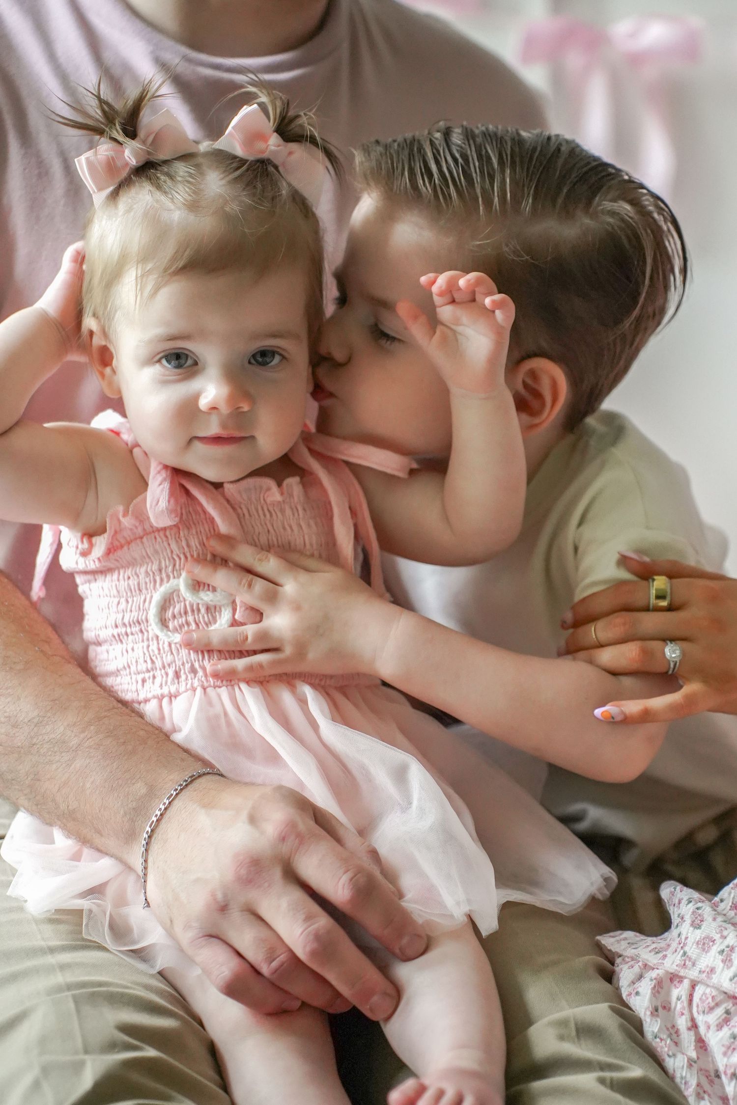 Sweet siblings share a tender moment as big brother gives a gentle kiss while dressed in matching pink and sage green outfits.