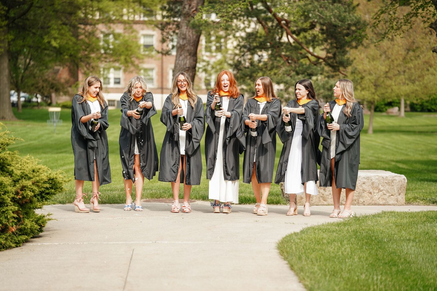 A group of bridesmaids in gray dresses holding bouquets pose together on a garden pathway in spring.