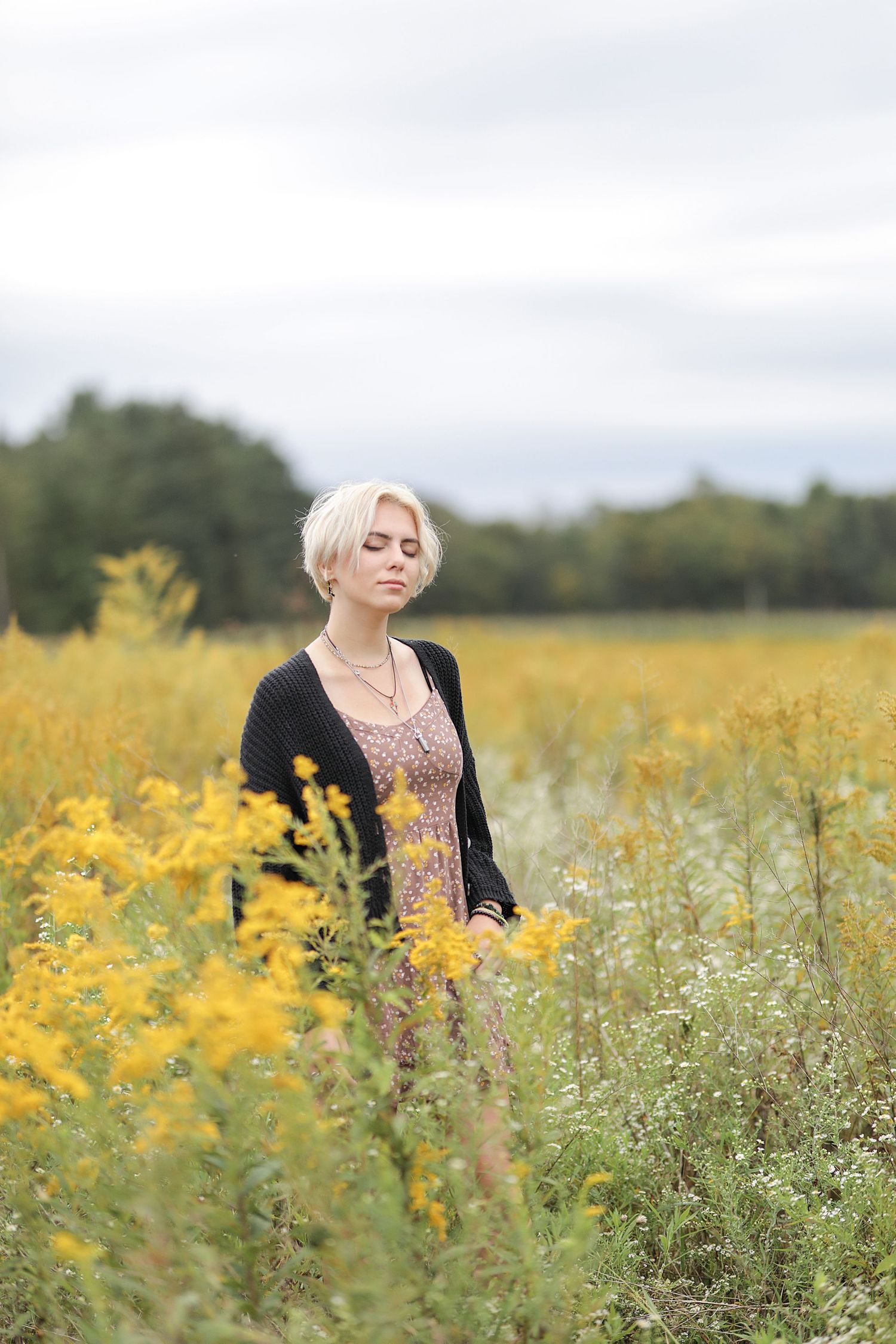 A figure stands in a blooming field of yellow wildflowers against a cloudy sky.