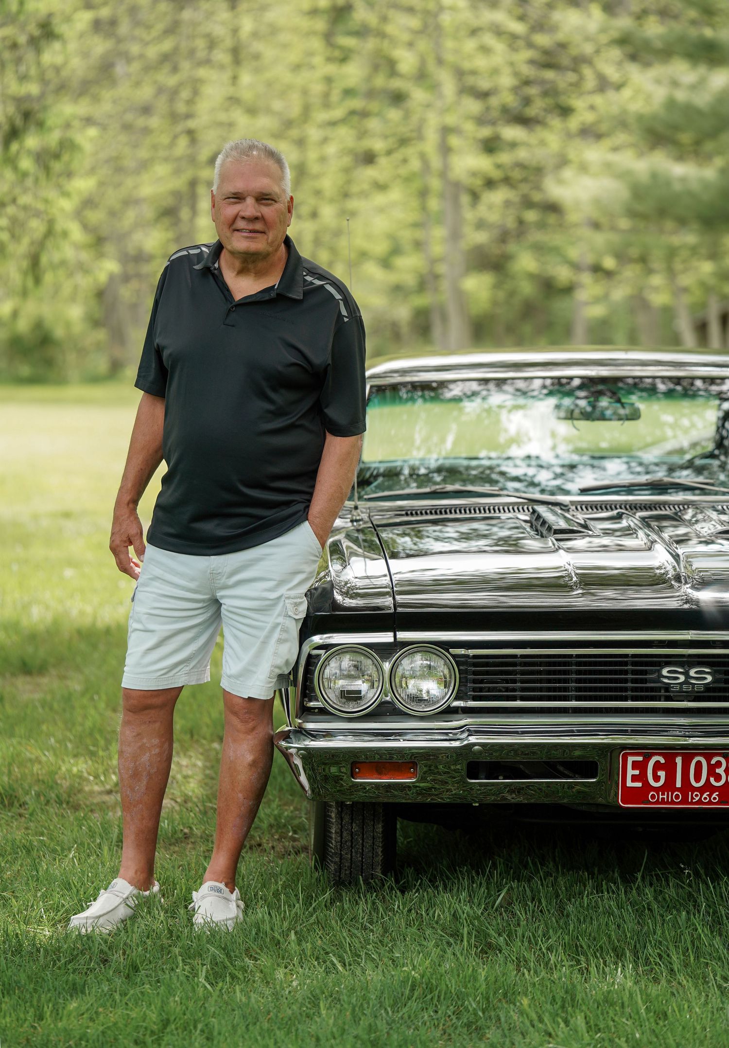 Classic Chevrolet SS car with chrome trim parked on grass with owner standing beside it on a sunny day.