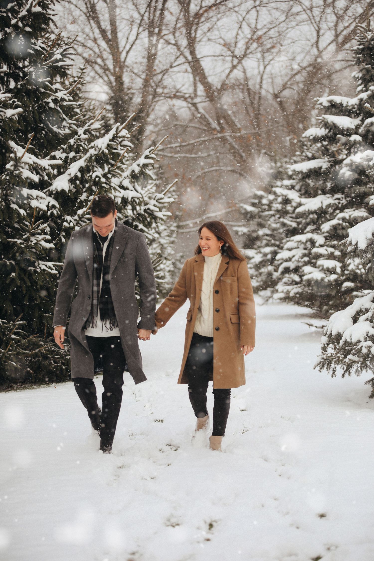Couple walking hand in hand through snow-covered evergreen trees in winter wonderland setting. Engagement photography in Cleveland Ohio.