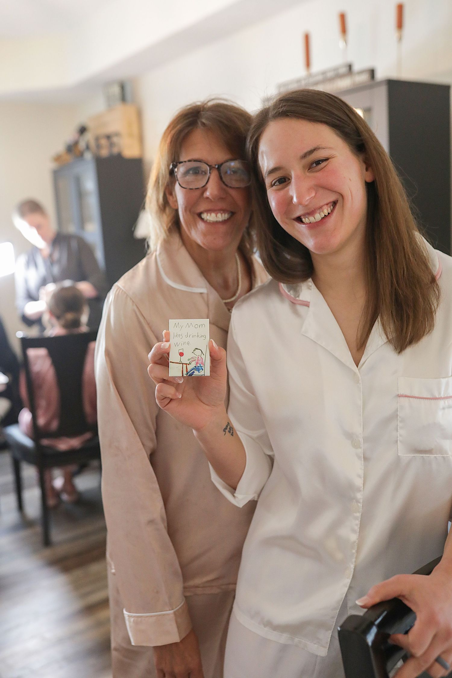 Two healthcare professionals in white and beige uniforms smile together in a medical setting.