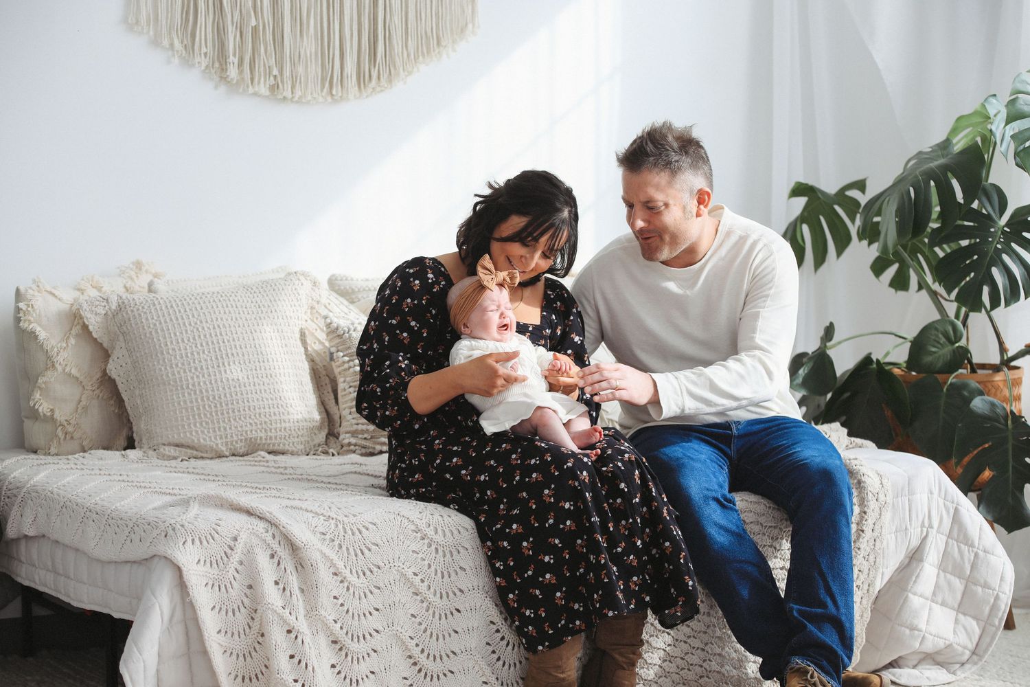 A series of intimate family moments captured in a bright, modern living room setting with soft white decor and natural light.