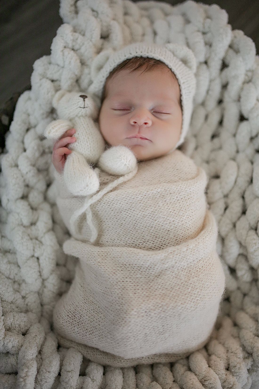 Sleeping newborn wrapped in soft white knit blanket on chunky knit backdrop. Newborn photographer Cleveland, Ohio.