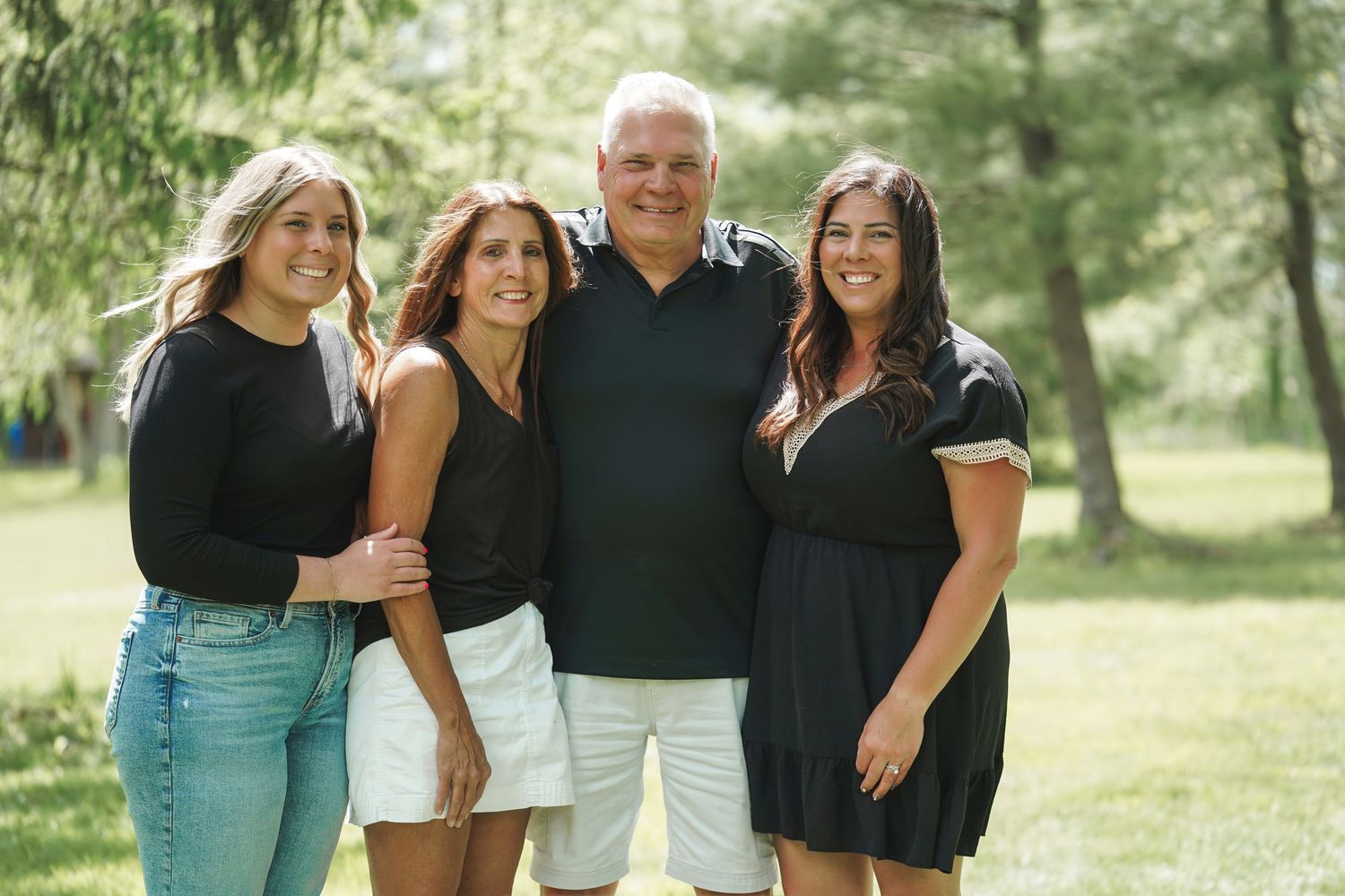 A happy family poses together outdoors in matching black and white outfits for a casual photo session in a park setting.