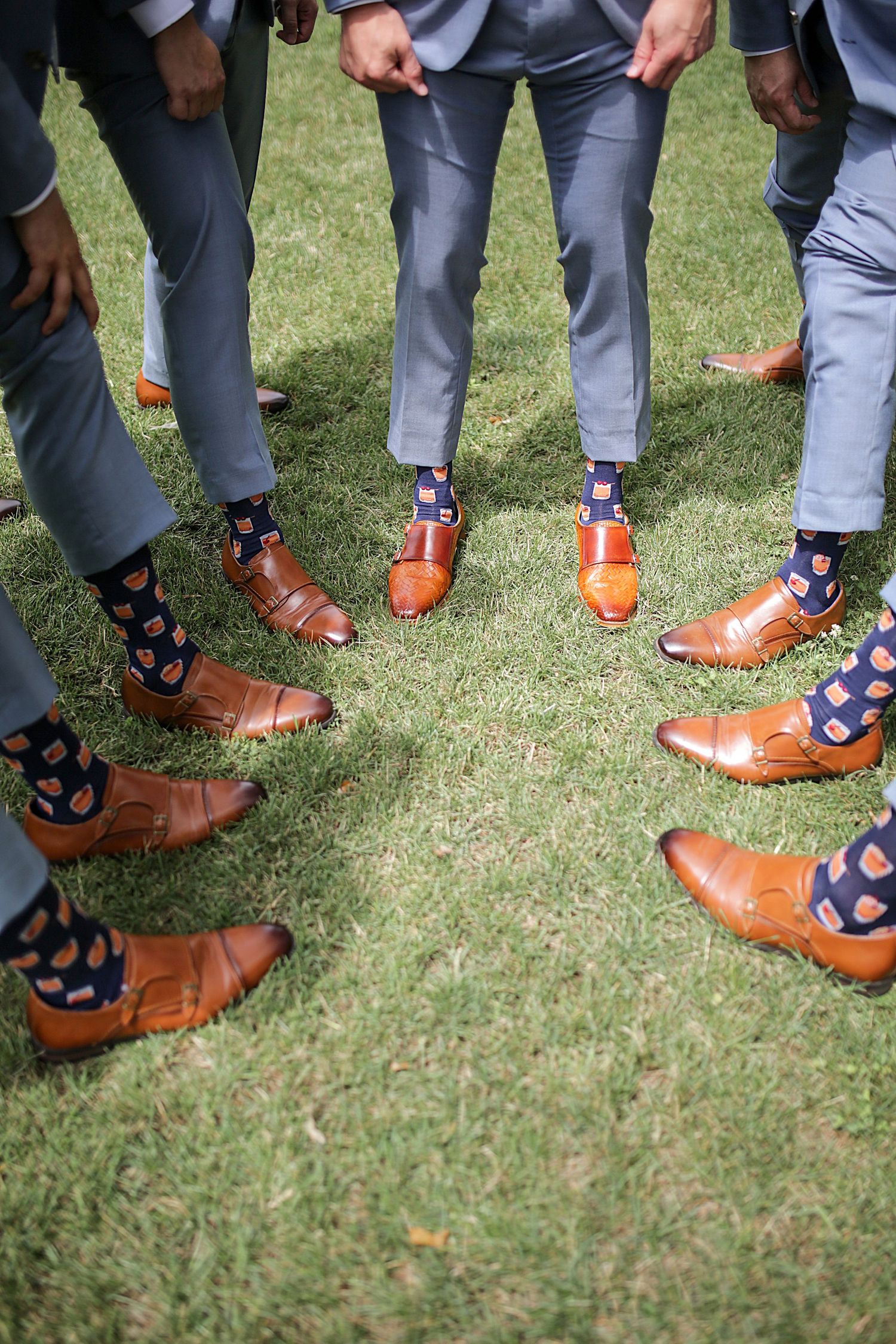 Close-up of groomsmen's brown leather dress shoes and colorful socks on grass.