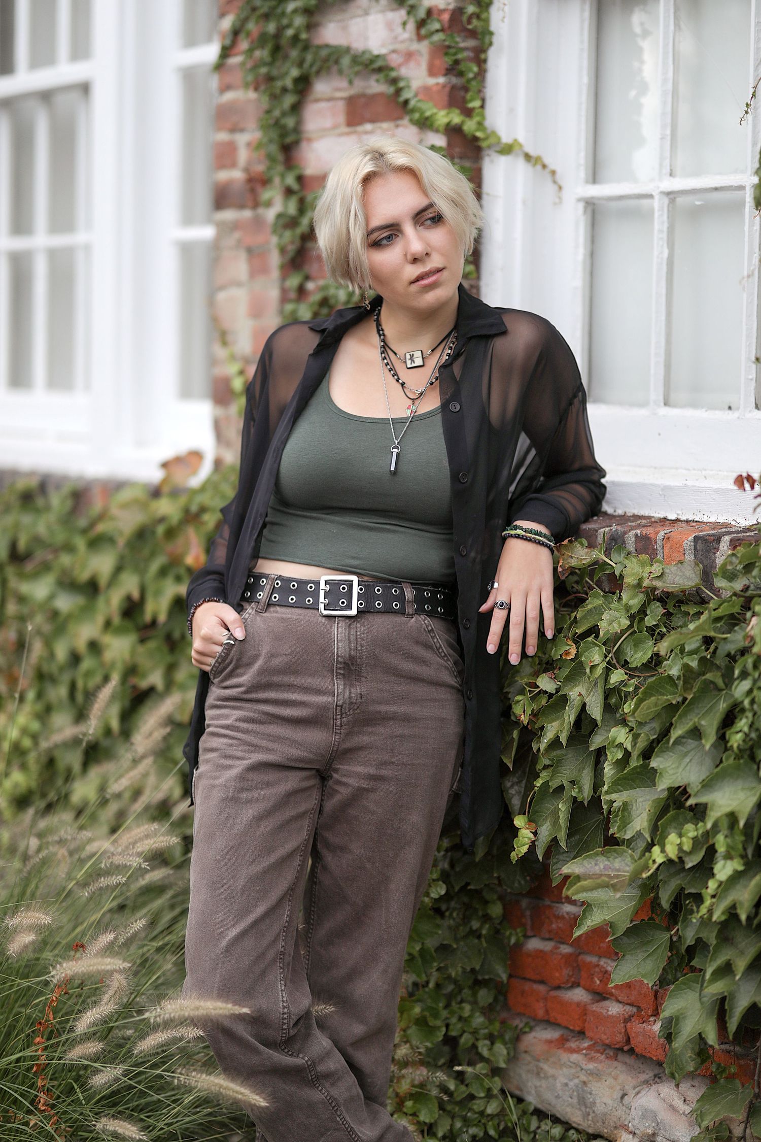 Four fashion outfit photos showcasing brown jeans and dark clothing against a brick wall with climbing ivy.