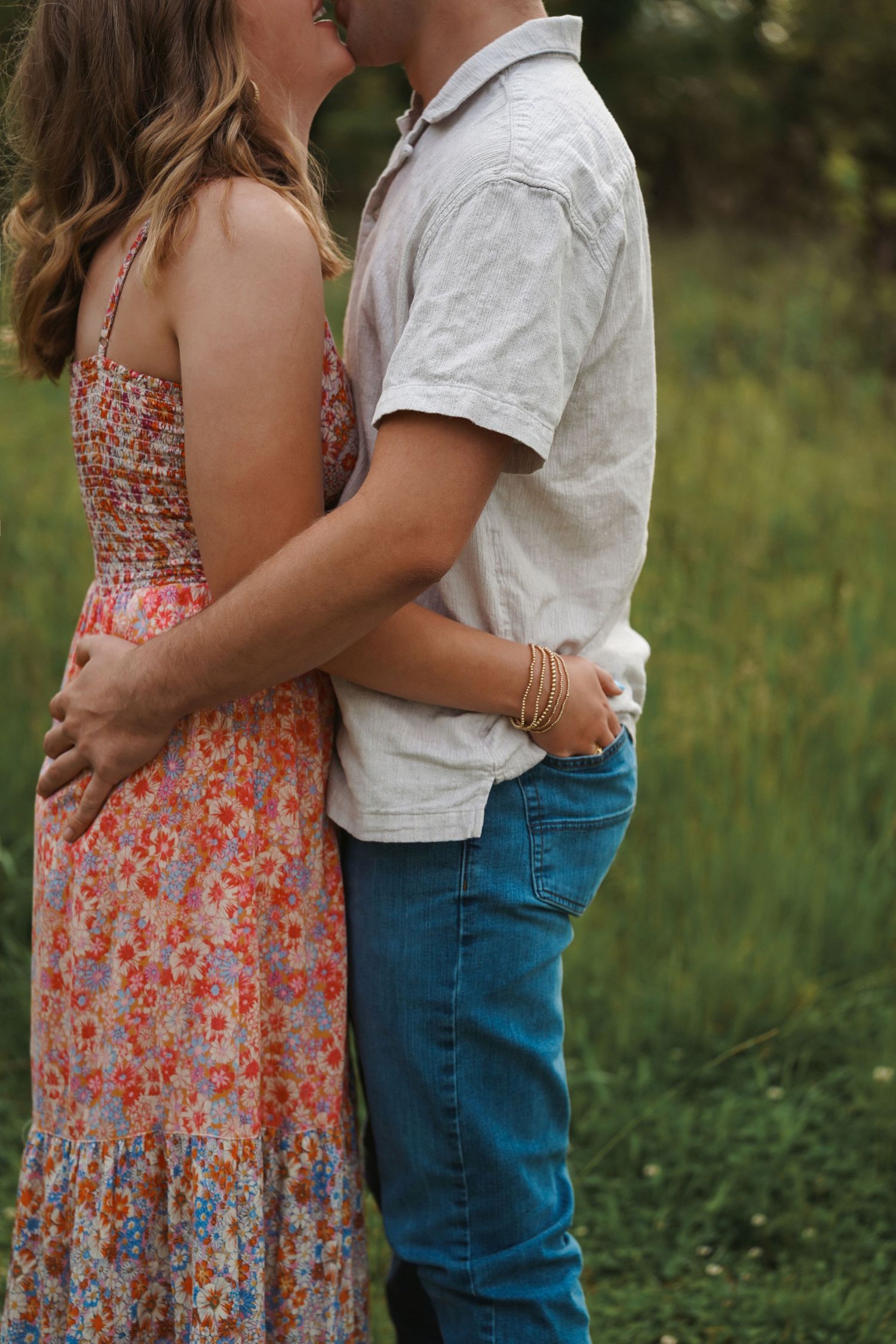 A couple embraces outdoors in casual attire during a romantic photoshoot in a grassy field.