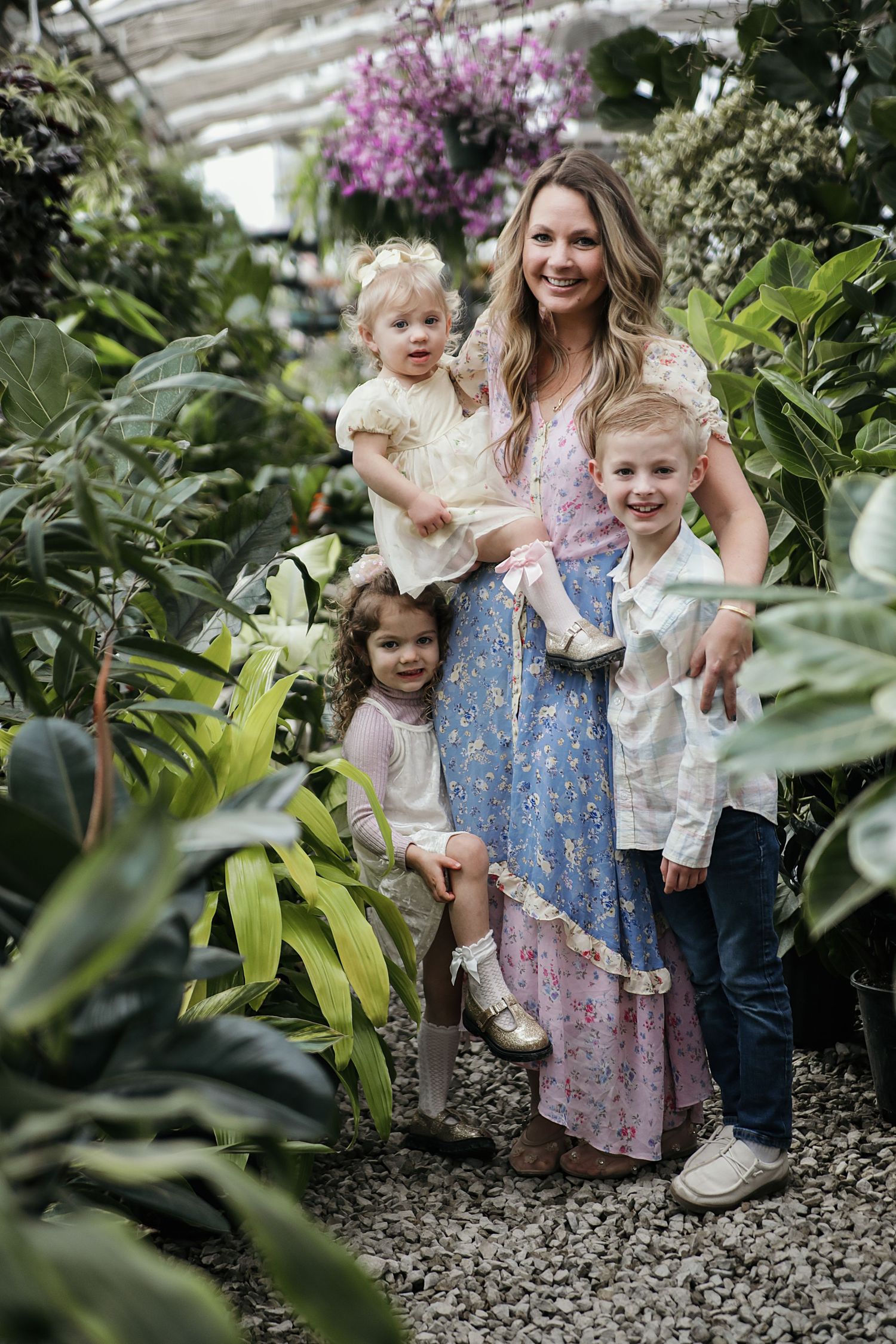 A candid family photo session in a garden featuring a woman and children among blooming purple flowers and greenery.