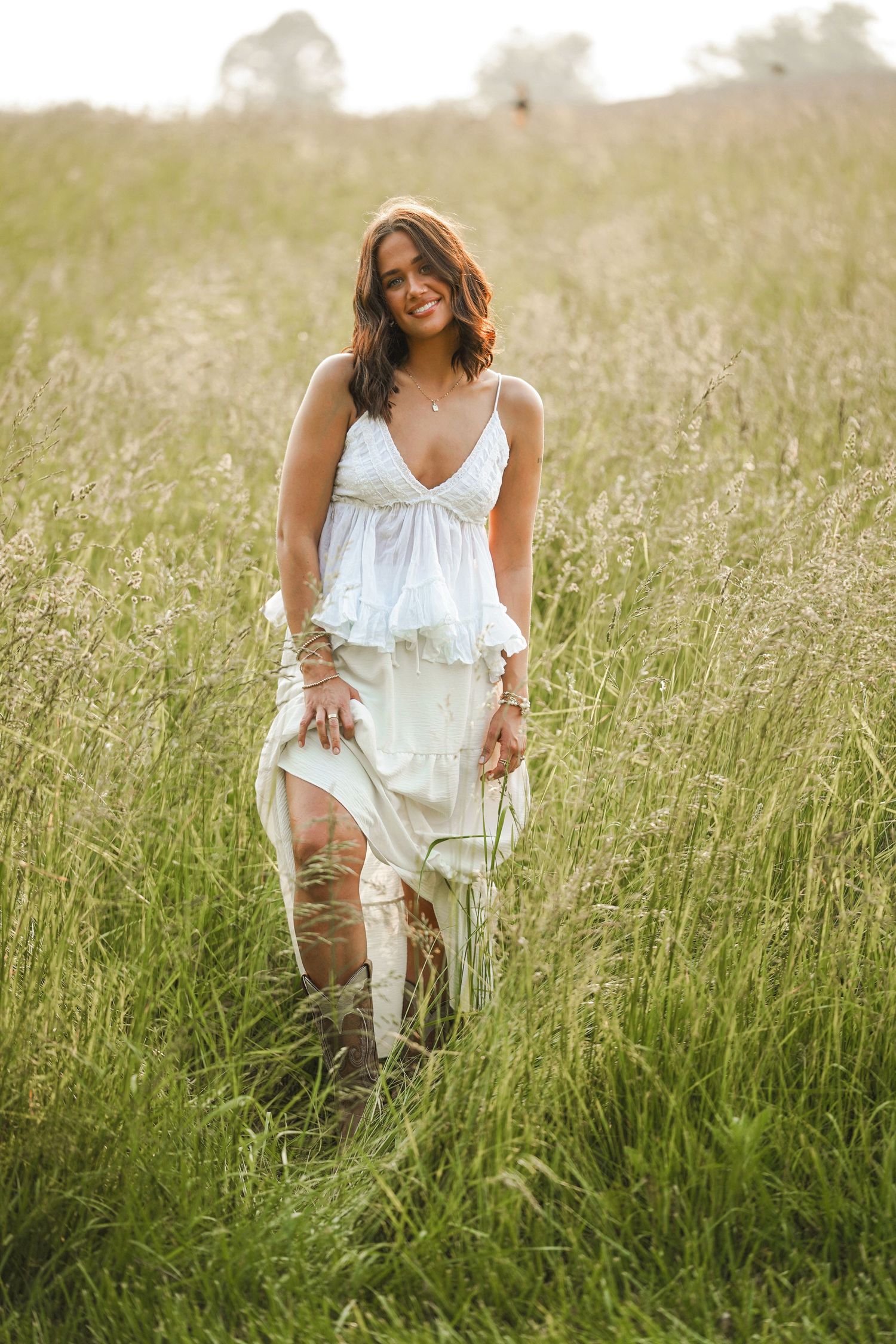 A white flowy dress billows in the breeze as someone walks through a sun-lit meadow of tall grass.