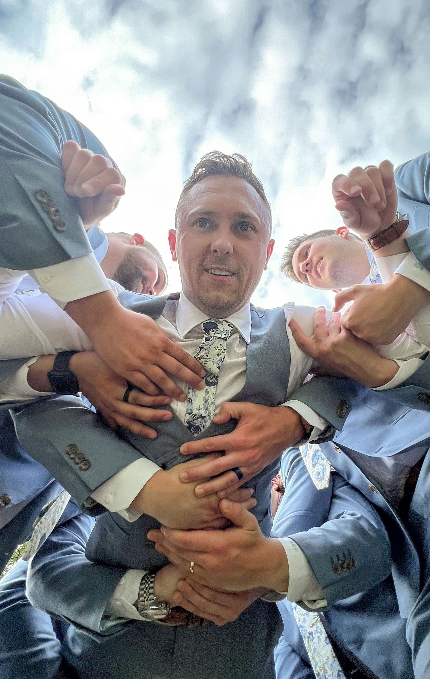 Playful groomsmen group photo with hands piled on groom in light blue suits.