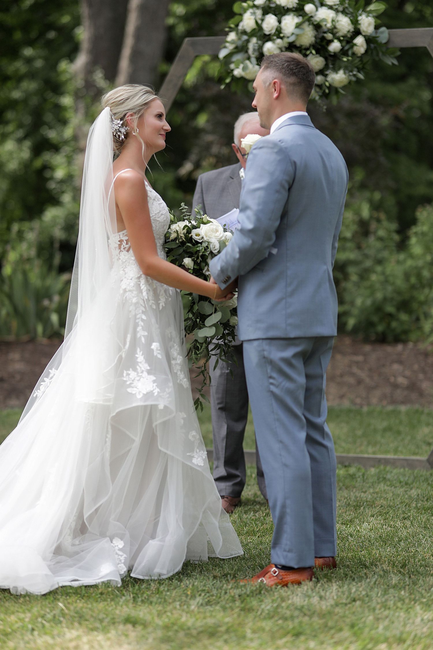 Outdoor wedding ceremony scene with floral arch and couple exchanging vows.