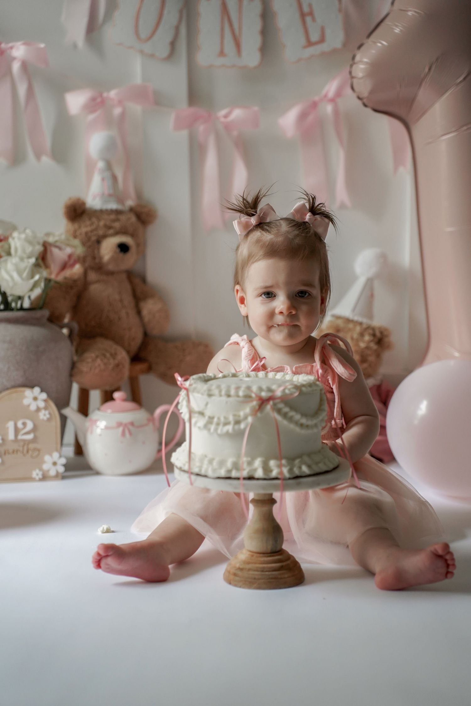 Soft pink baby cake smash photography setup with vintage props and teddy bears for a first birthday celebration.