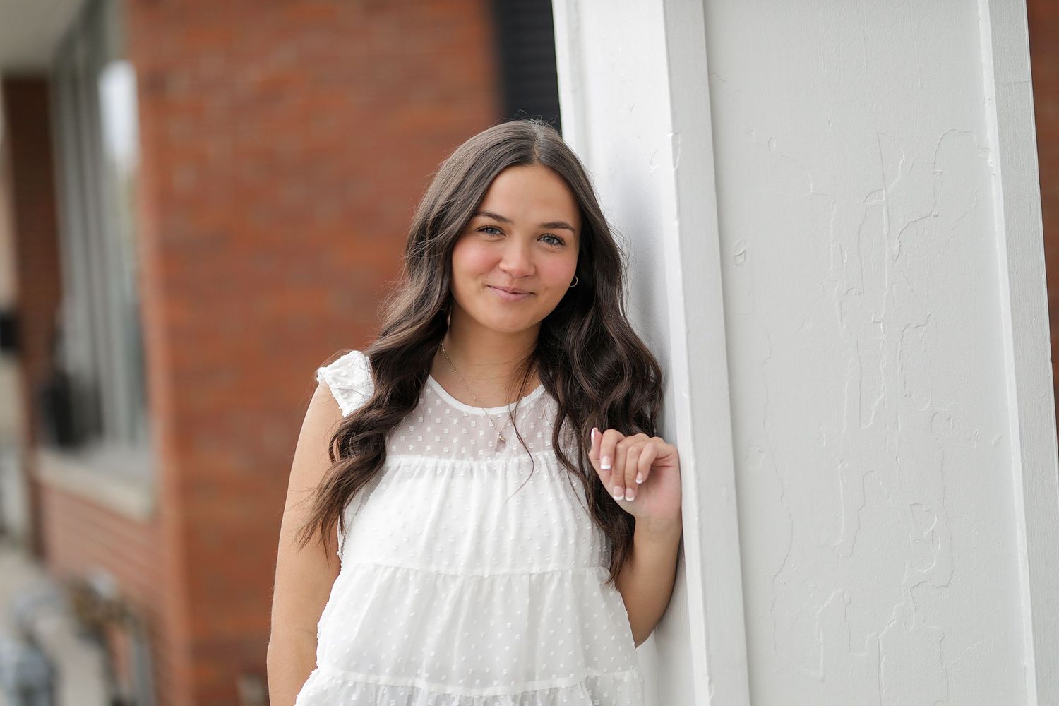 Young woman in white lace dress and dark hair poses by white pillars outdoors.