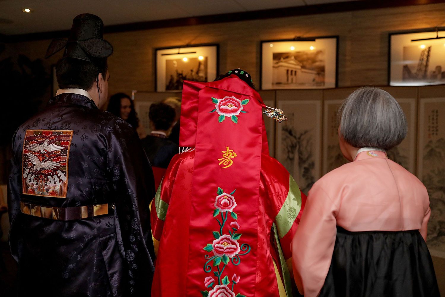 Traditional Korean hanbok garments on display, featuring a bright red embroidered robe with decorative patterns in a gallery setting.