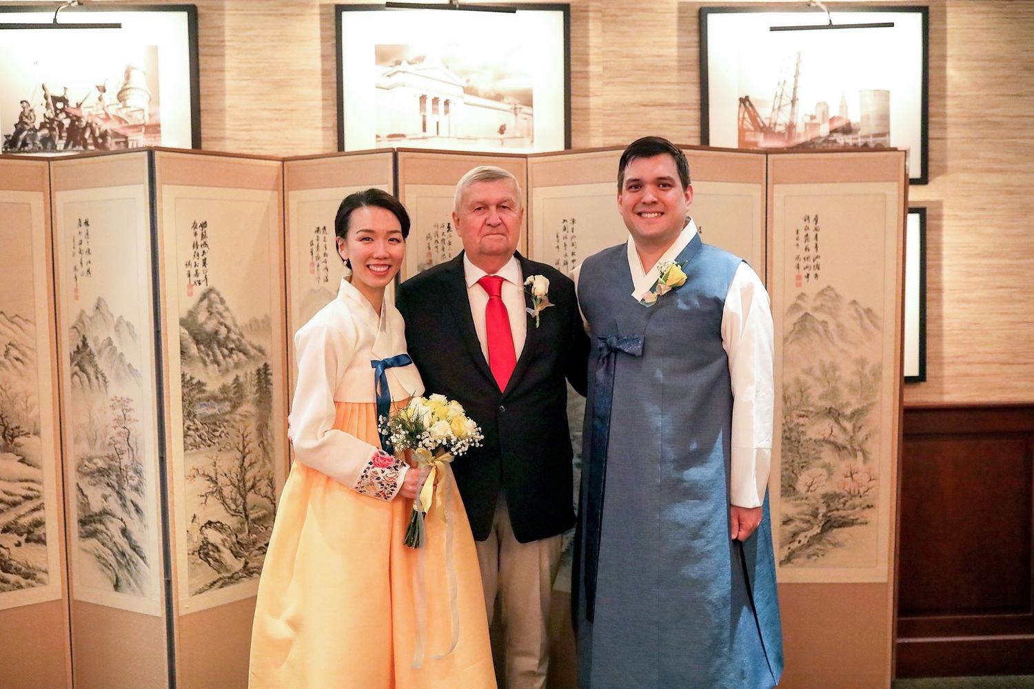 People posing in front of decorative Asian folding screens at a formal event, with traditional dress and formal attire.