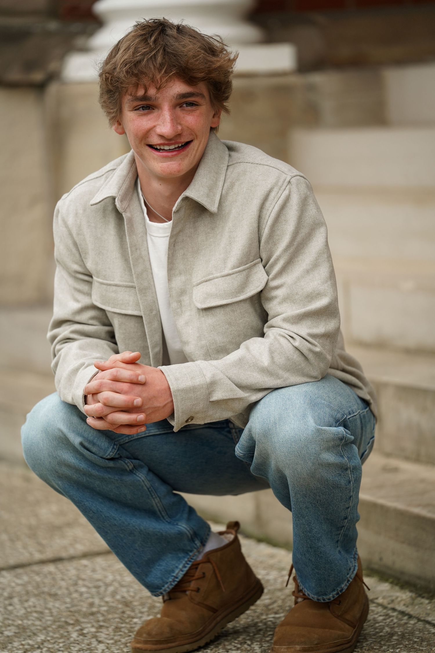 Casual senior portrait of student in light jacket sitting on concrete steps.