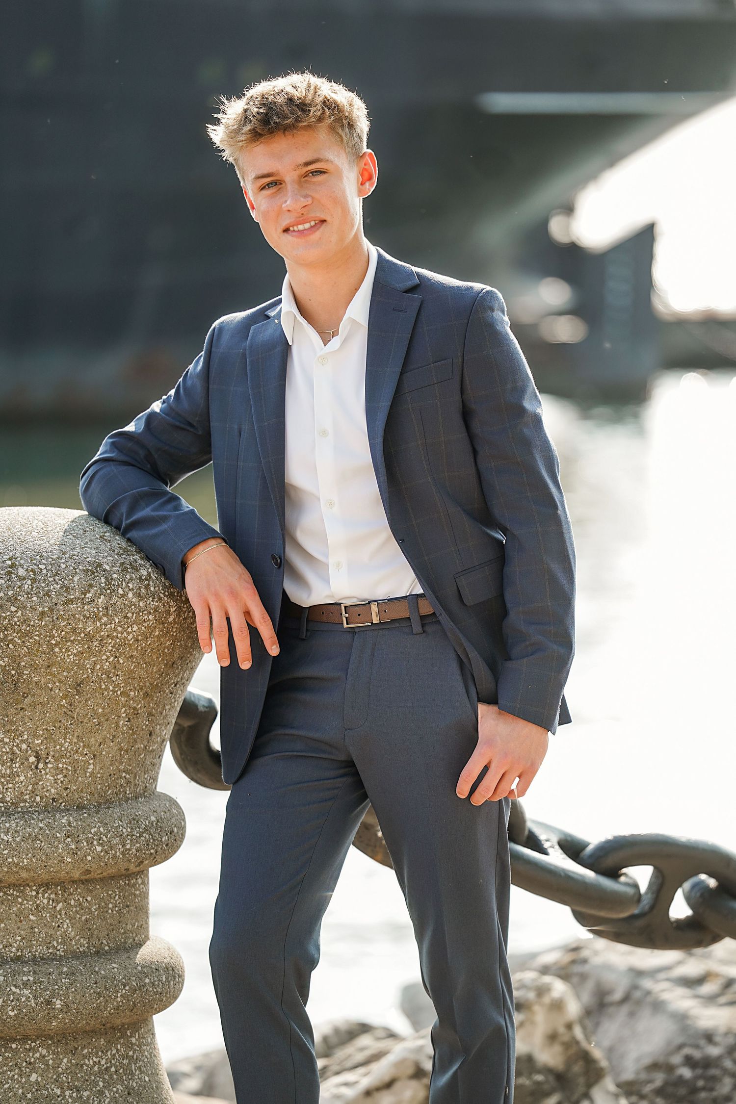 Professional portrait of someone in a navy blue suit and white dress shirt posing outdoors by an anchor chain.