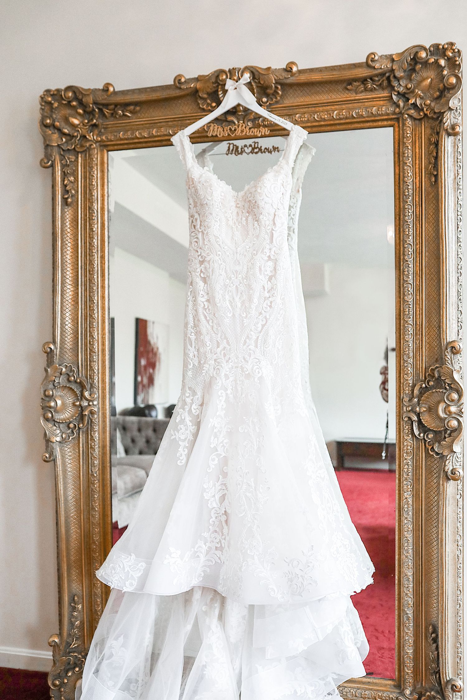 Elegant white lace wedding dresses hanging on display against ornate gold-framed mirrors in a bridal boutique.