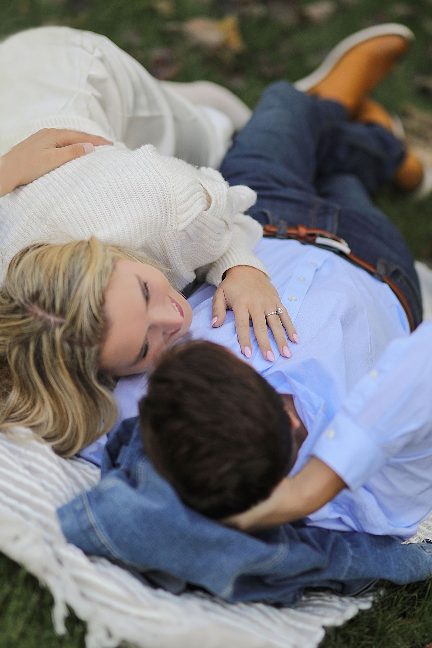 A couple lies together relaxing on a blanket in the grass on an autumn day.
