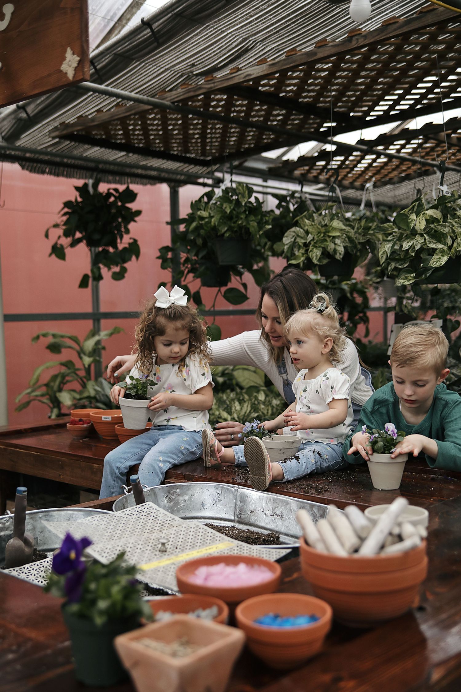 Children learning gardening and planting activities with terracotta pots and soil on a covered outdoor patio table.