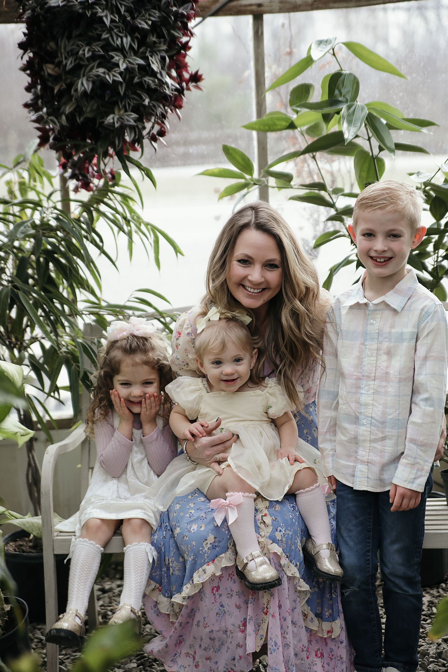 A family poses together in a greenhouse surrounded by lush greenery and plants.