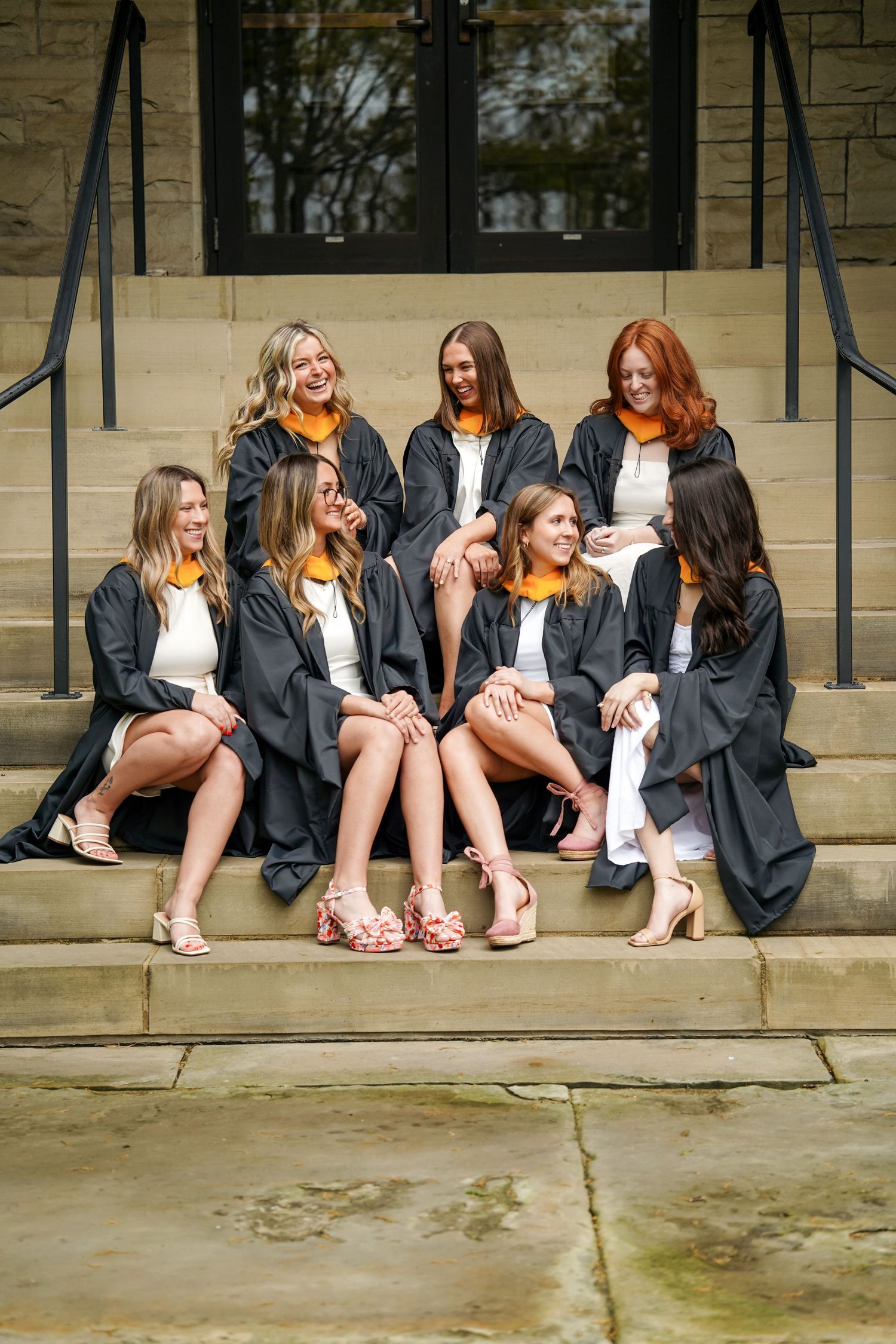 A panoramic photo sequence showing graduates in black gowns sitting on stone steps and displaying their colorful shoes.