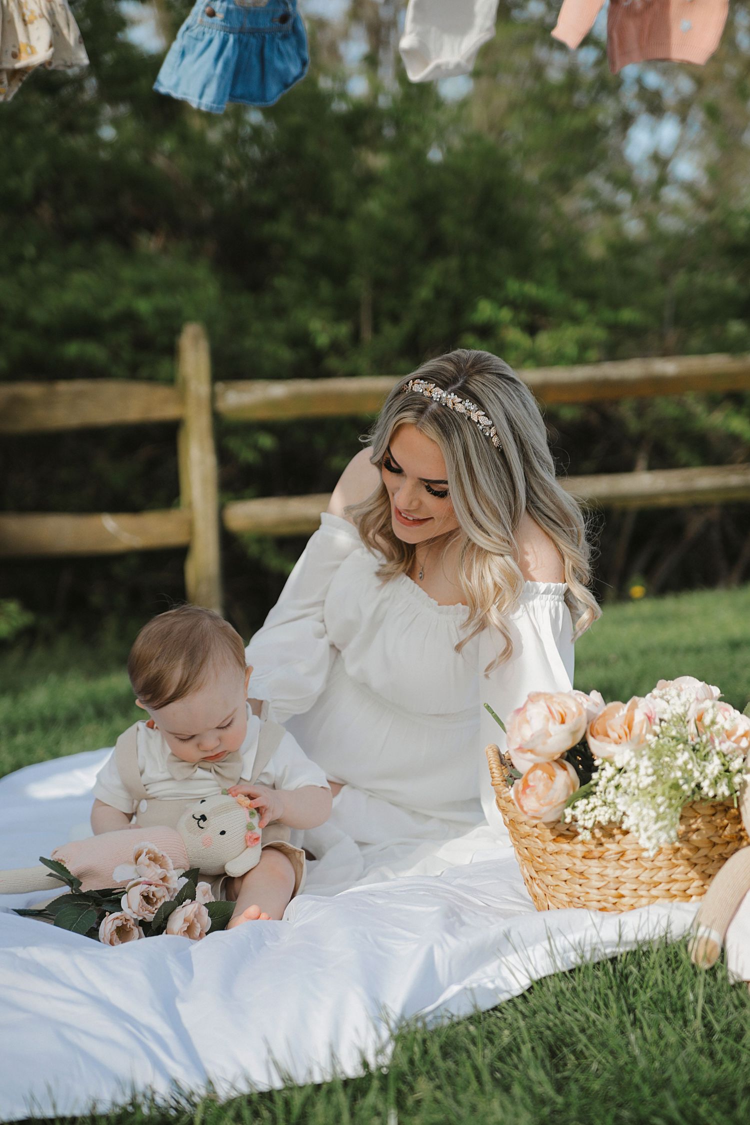 Parent and child in white dresses sharing an intimate moment while sitting together on a picnic blanket in a grassy field.