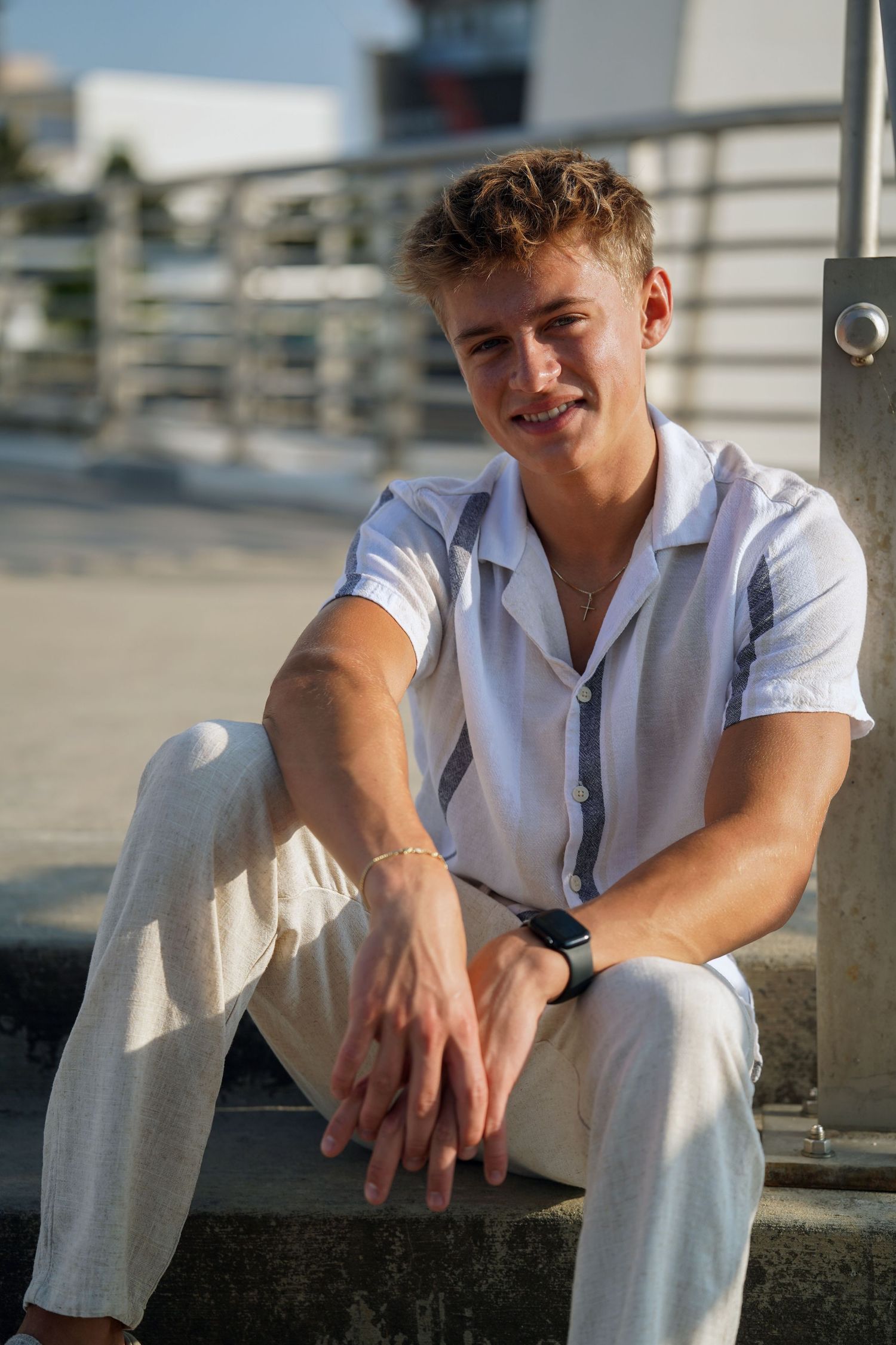 Young person in an all-white outfit sits casually on steps outdoors during golden hour sunlight.