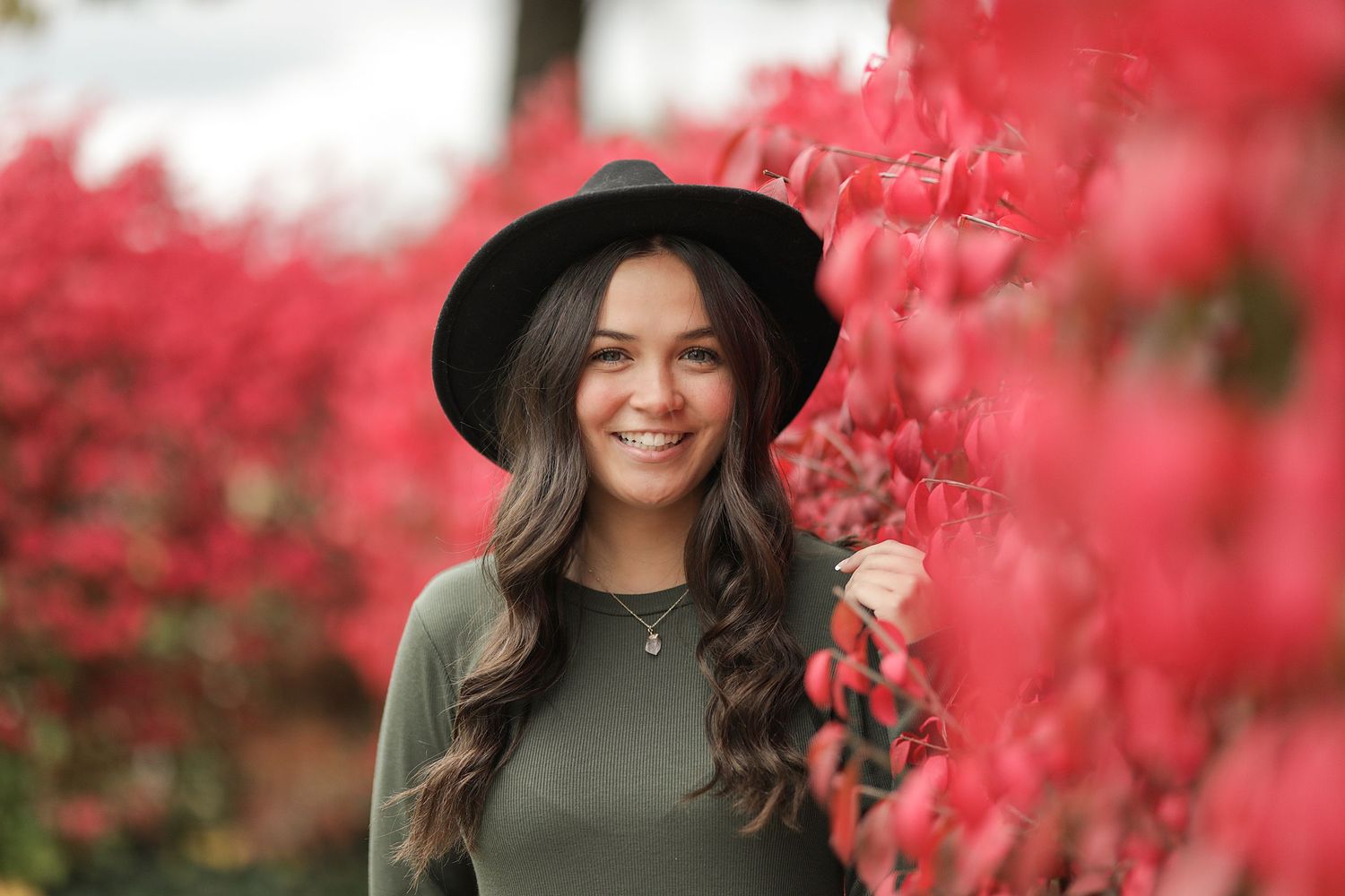 Portrait photography against vibrant red autumn foliage with soft natural lighting and bokeh background effect.