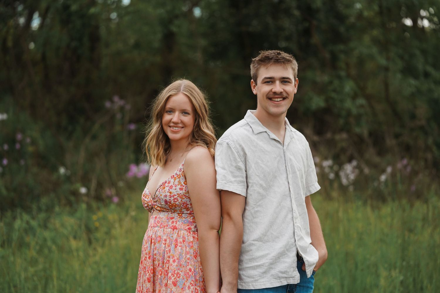 A couple shares a laugh together while posing in a lush green meadow during golden hour.
