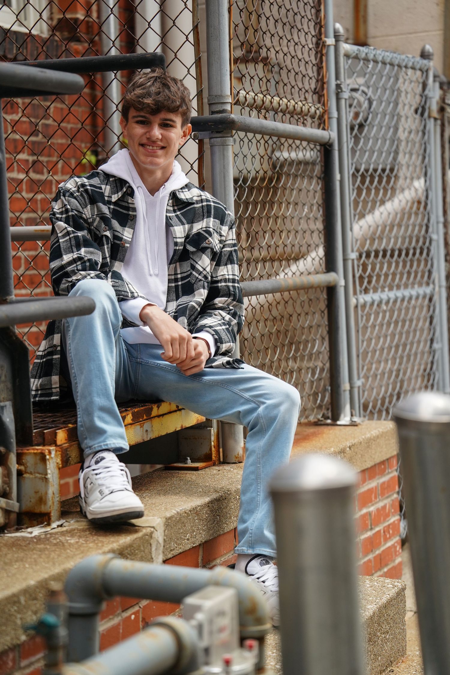 Casual portrait showing someone seated on brick steps wearing plaid flannel shirt, light jeans and sneakers.