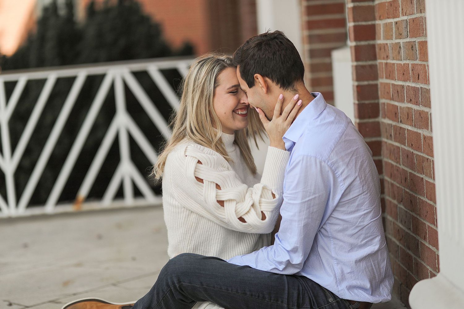 A couple shares an intimate moment while sitting together against a brick wall outdoors.