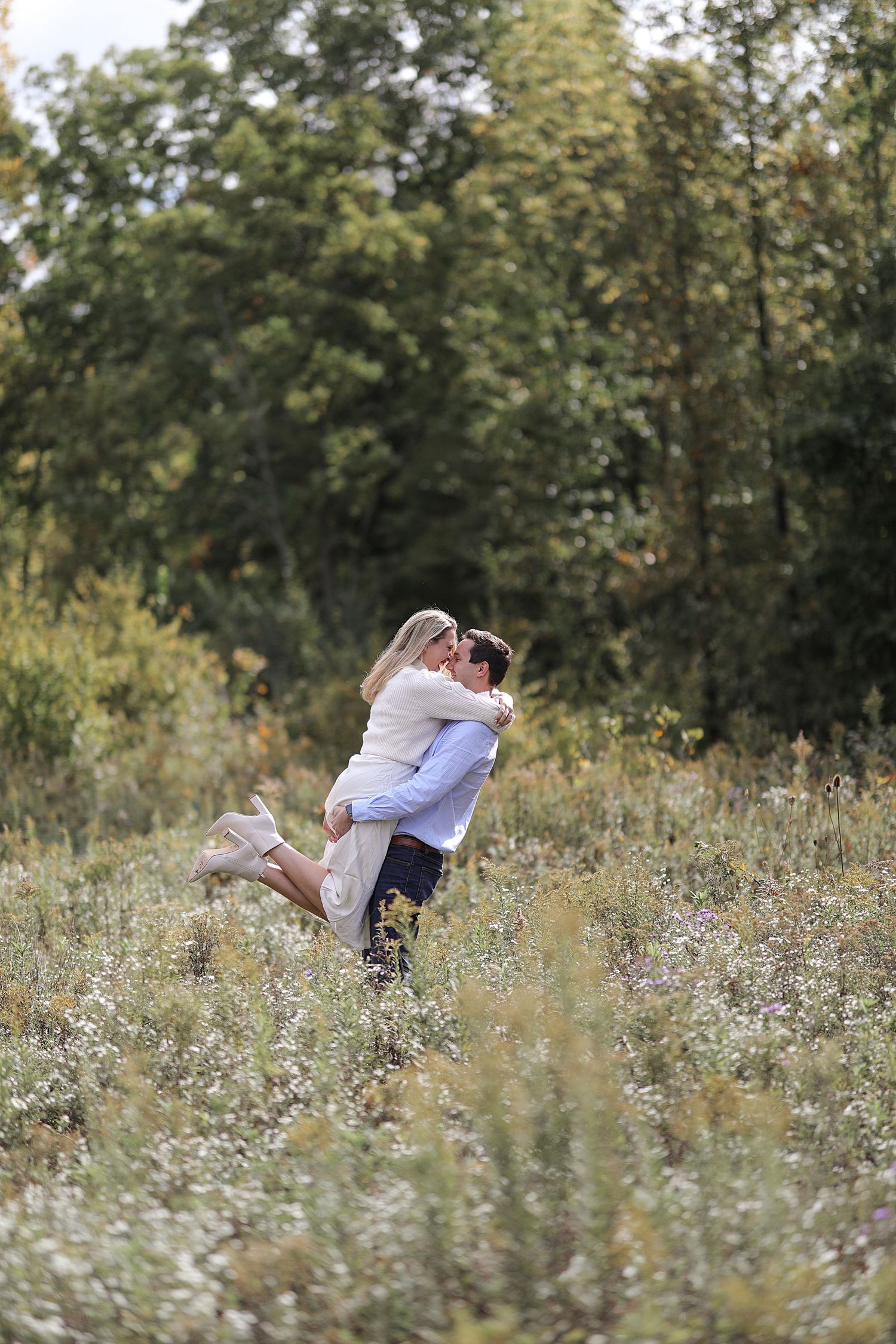 A romantic couple embraces in a dreamy summer meadow filled with delicate wildflowers and soft natural lighting.