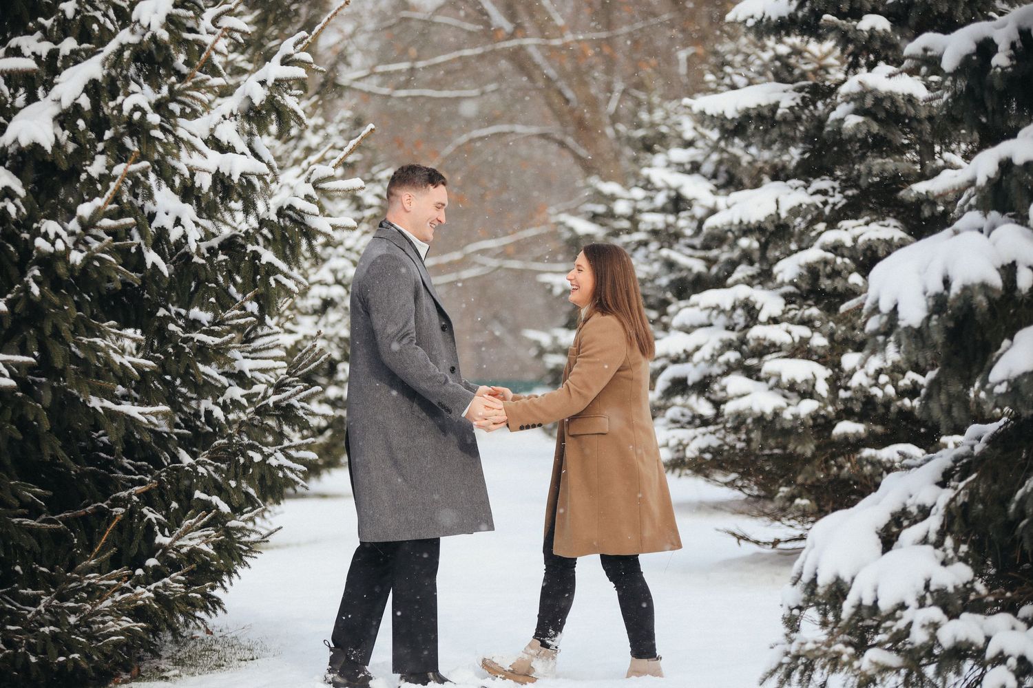 A couple shares a romantic moment among snow-covered evergreen trees in a winter forest setting.