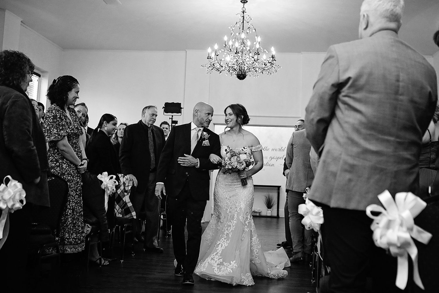 Wedding guests dance and celebrate on an elegant ballroom floor under crystal chandeliers during a reception.