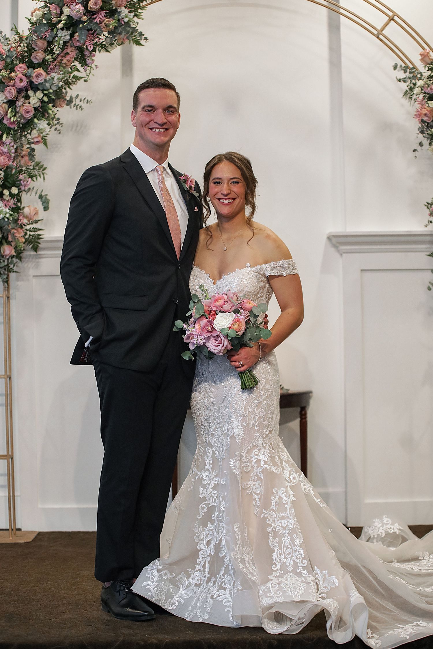 Elegant wedding couple poses under floral arch in series of romantic portraits.