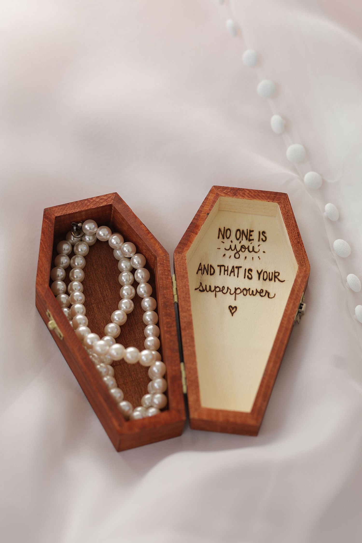 Pearl necklace inside wooden coffin-shaped box with handwritten note on the lid.