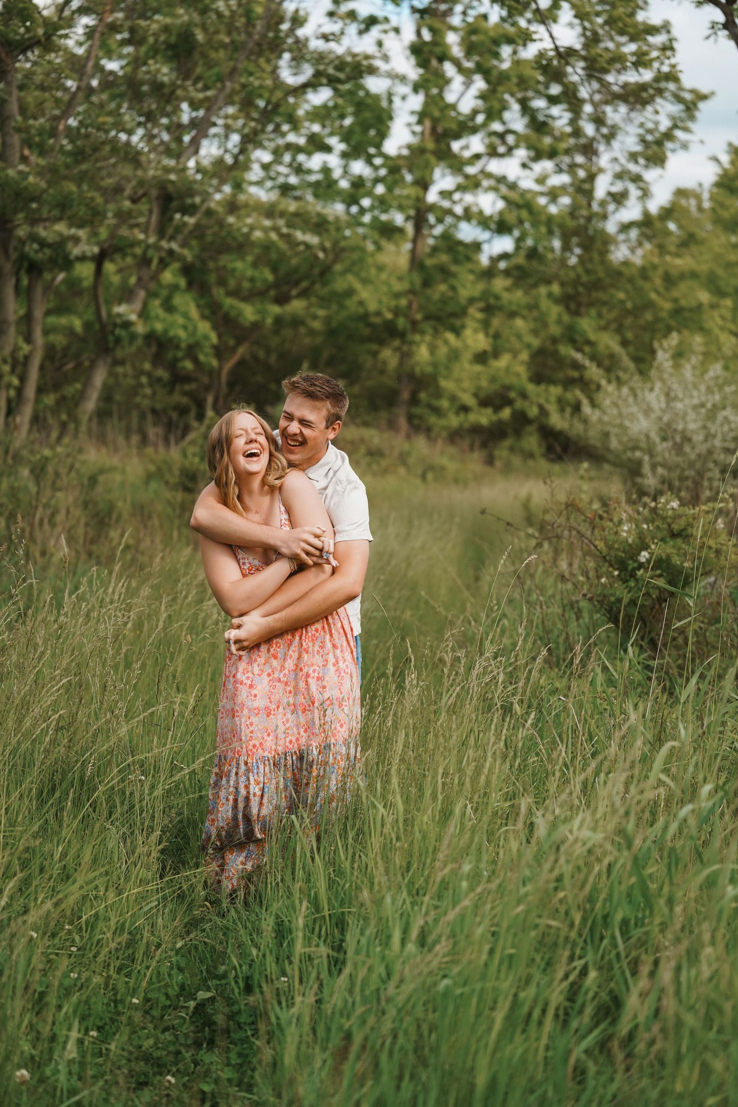 A joyful couple shares a tender moment while standing together in tall grass during a golden hour photoshoot.