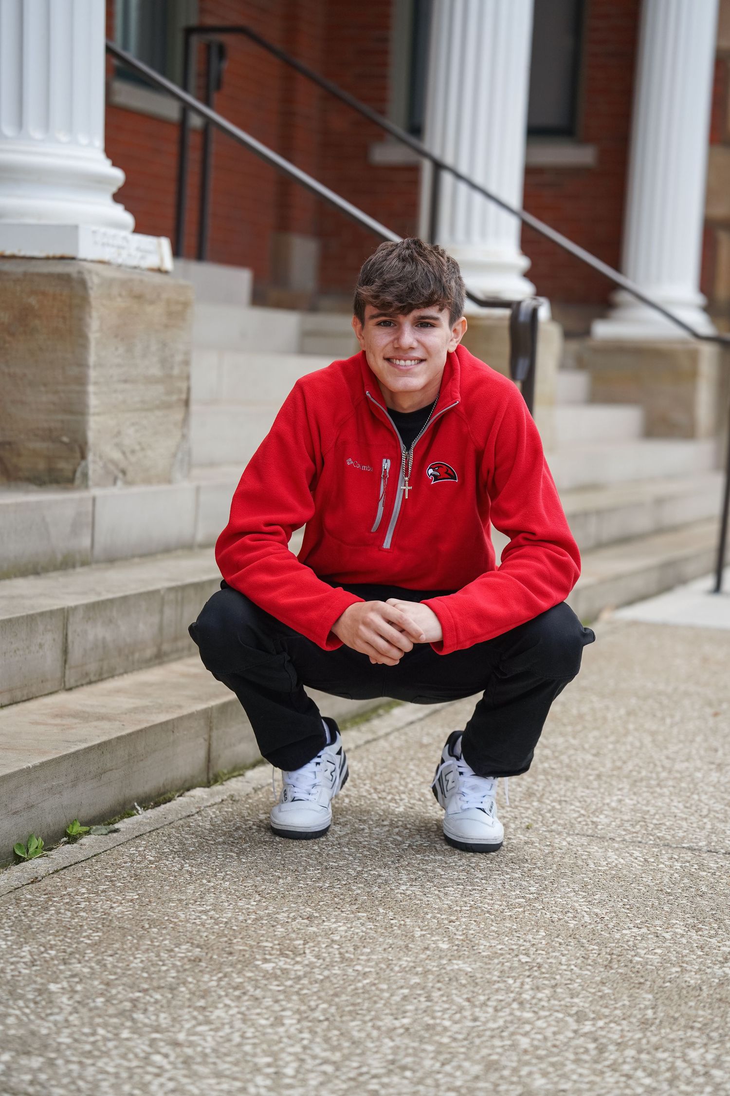 Person in red Columbia fleece jacket crouches on textured concrete steps near white columns.