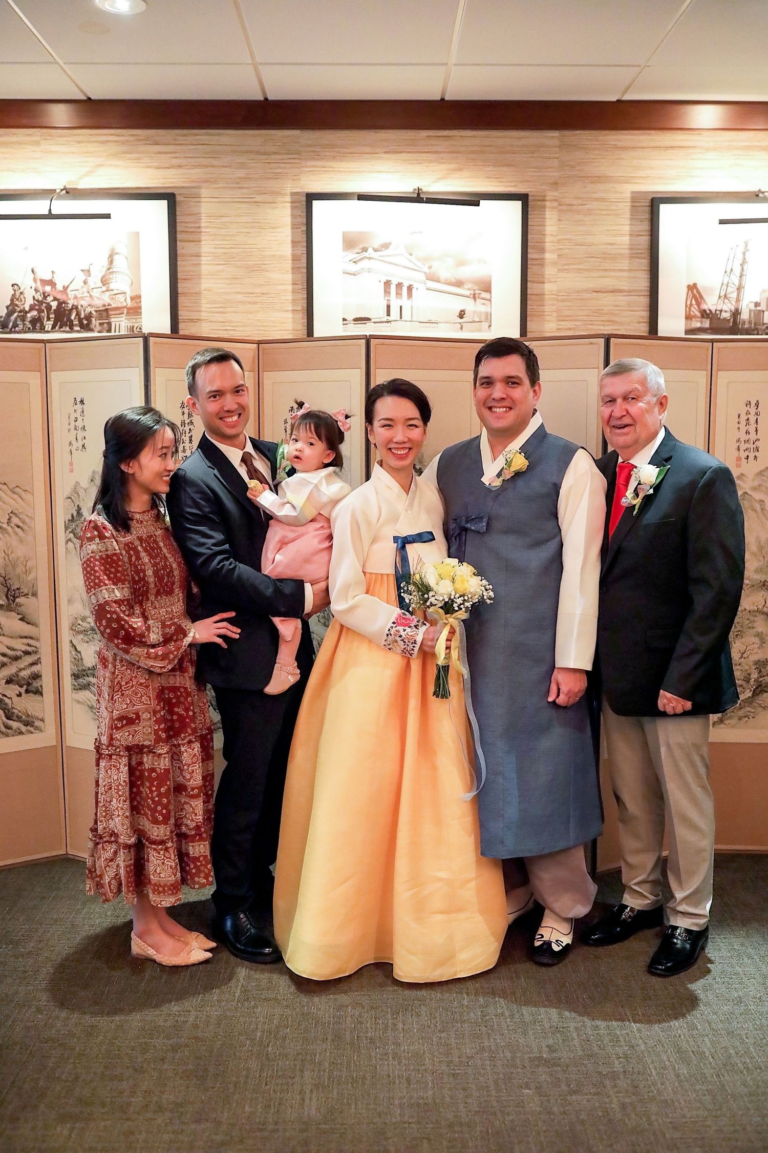 A group in formal attire including yellow gowns and suits pose for photos in a gallery with framed artwork on the walls.