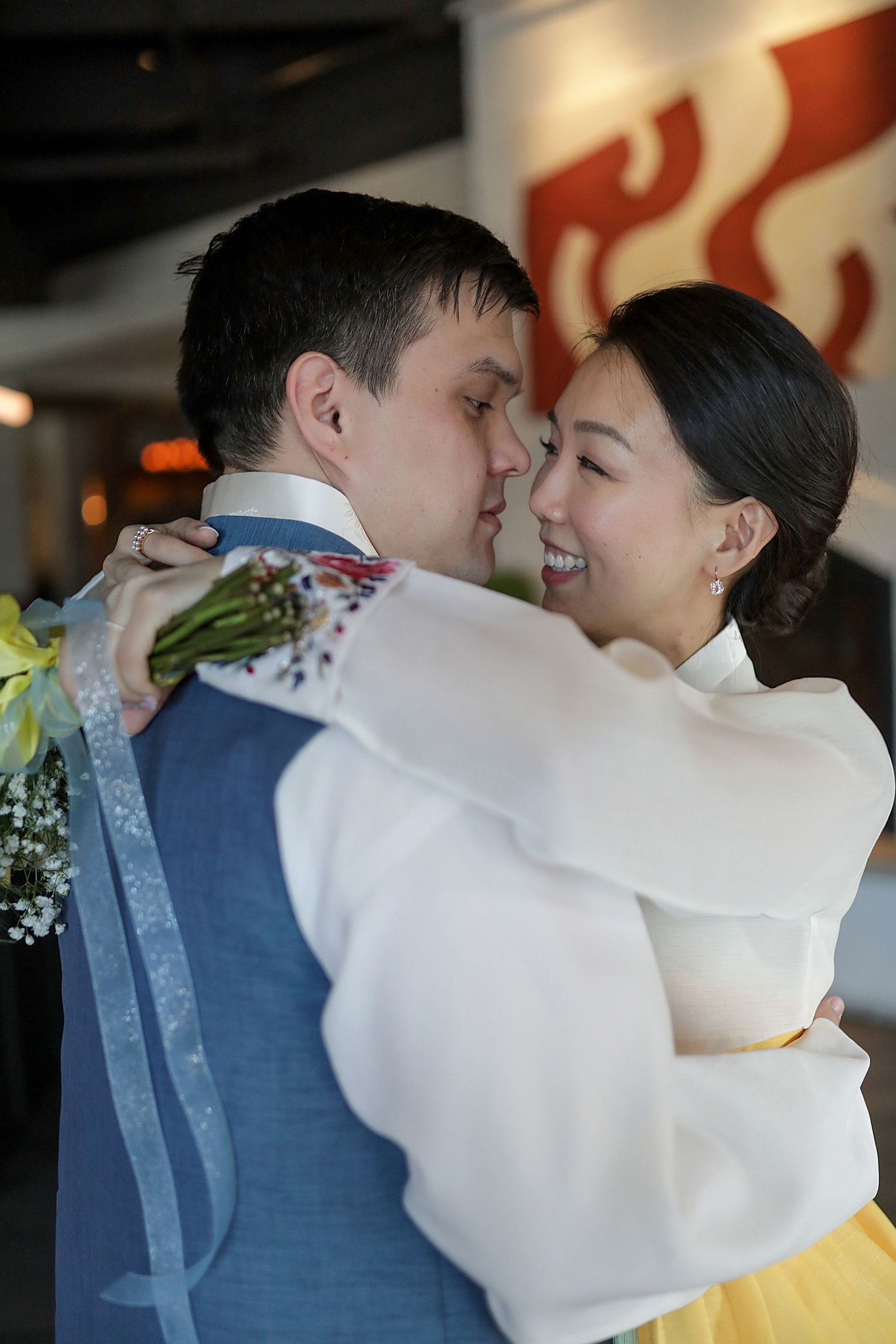 A joyful couple in traditional Korean hanbok attire embrace during what appears to be a wedding celebration.