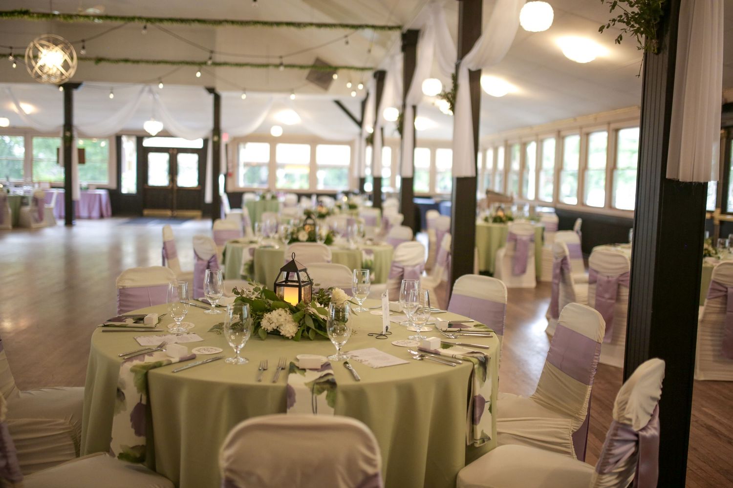 Elegant wedding reception venue with round tables covered in sage green linens and white chair covers.