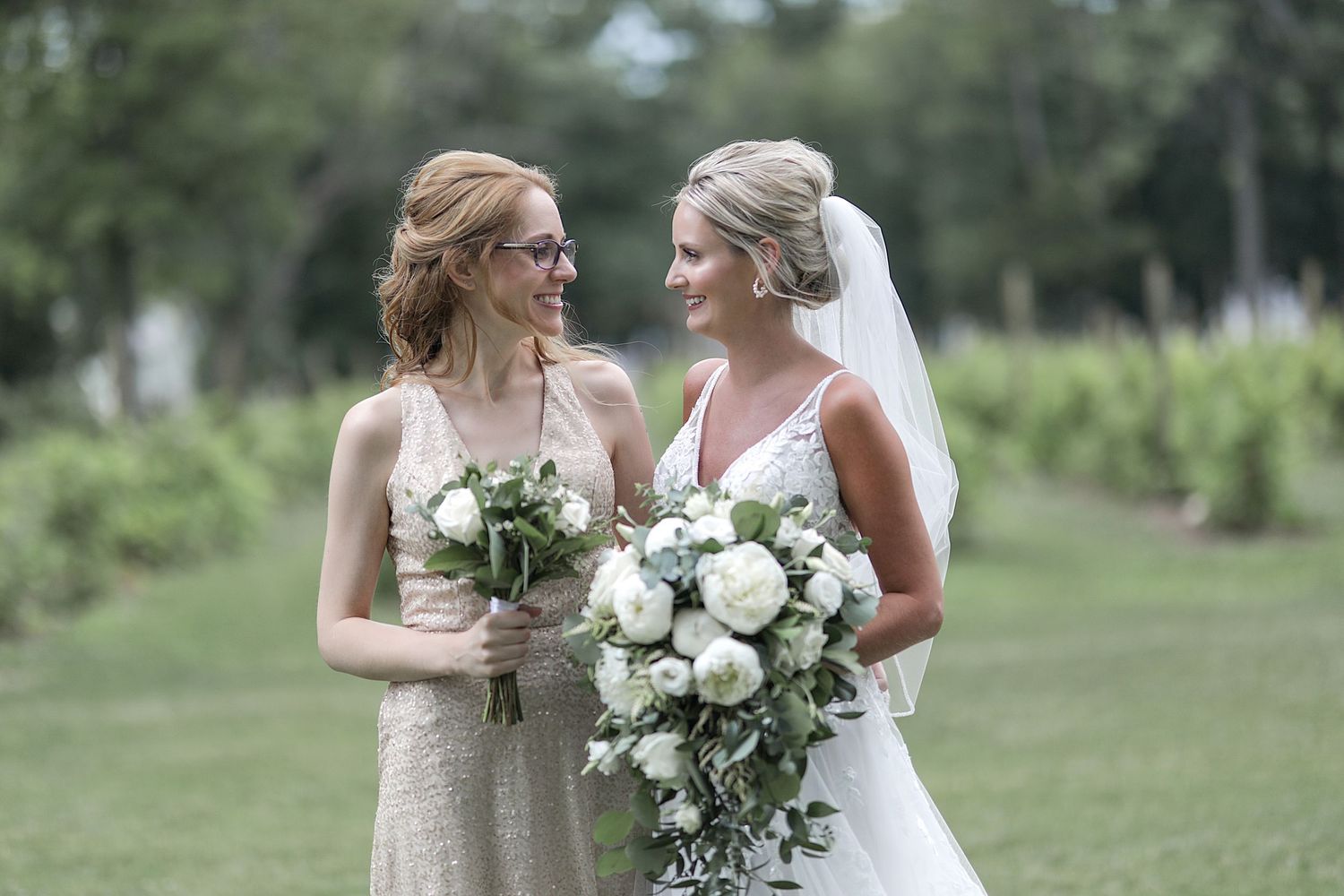 Wedding party members holding white floral bouquets at outdoor garden venue.
