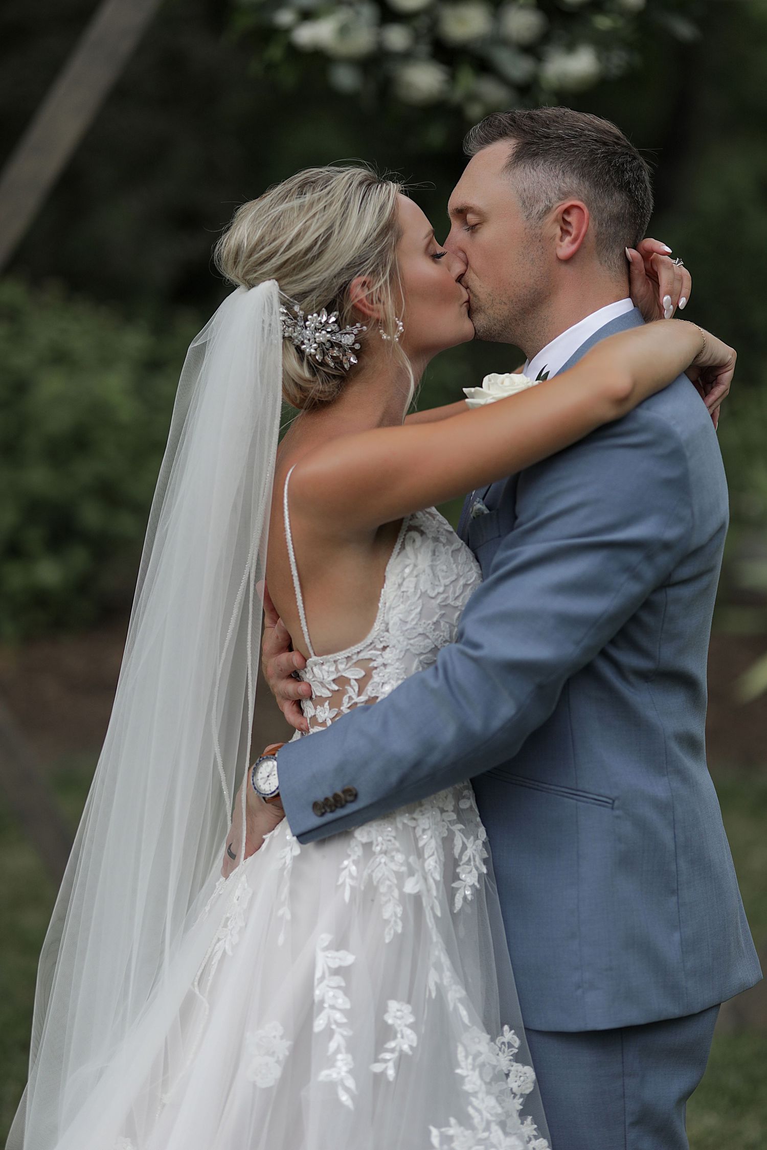 A romantic wedding kiss captured between newlyweds against a garden backdrop.