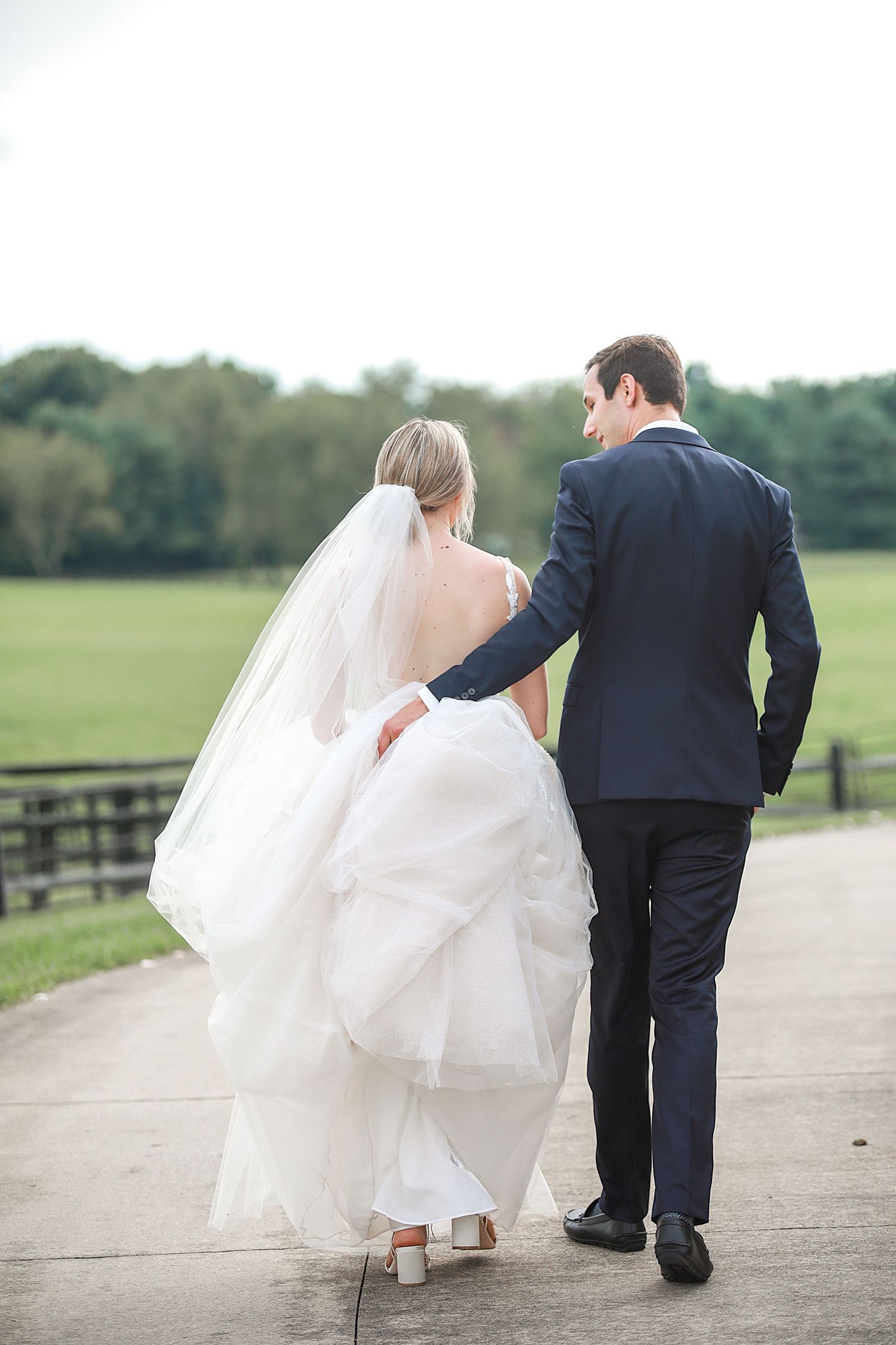 Newlyweds walk hand in hand down a country path with bride's dress flowing behind them. Cleveland wedding photographer.